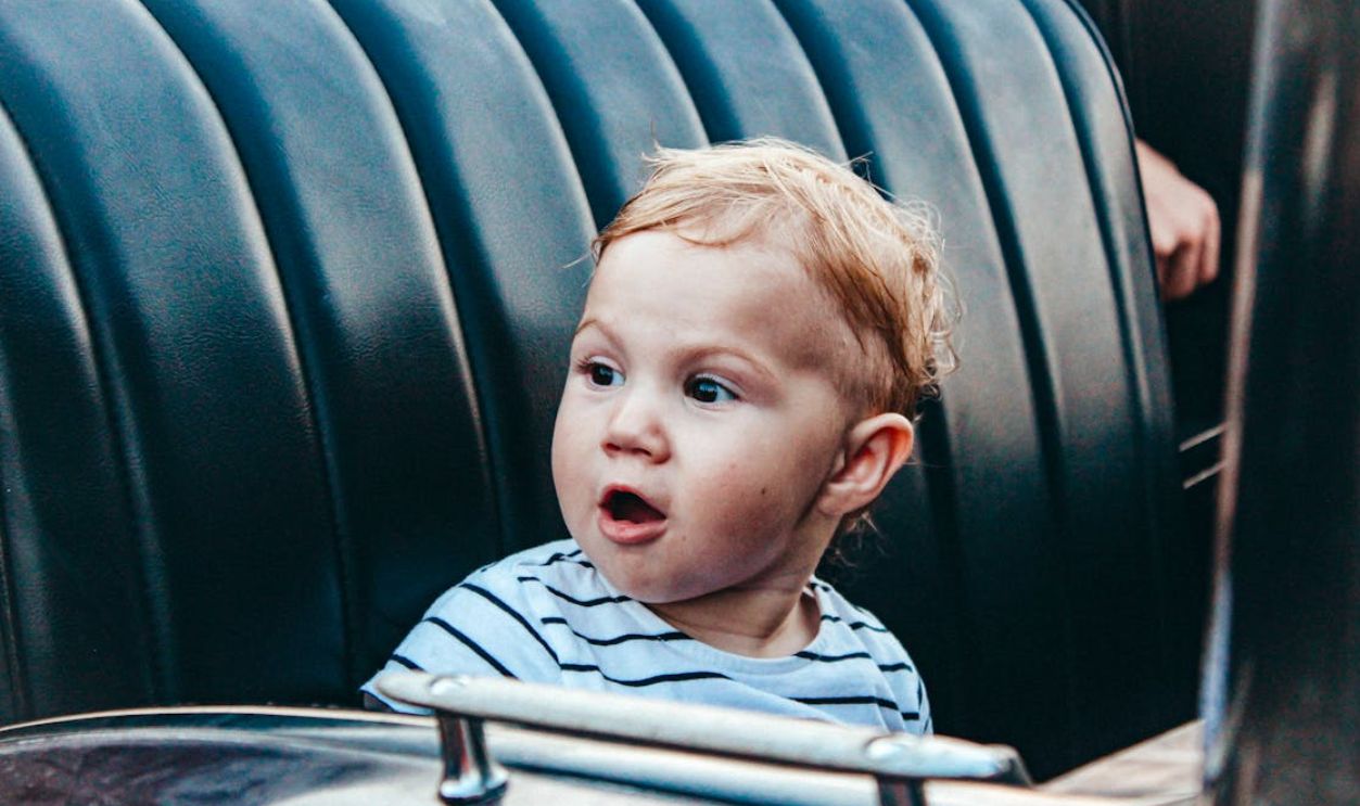 Cute child with surprised expression sitting in a car seat wearing a striped shirt