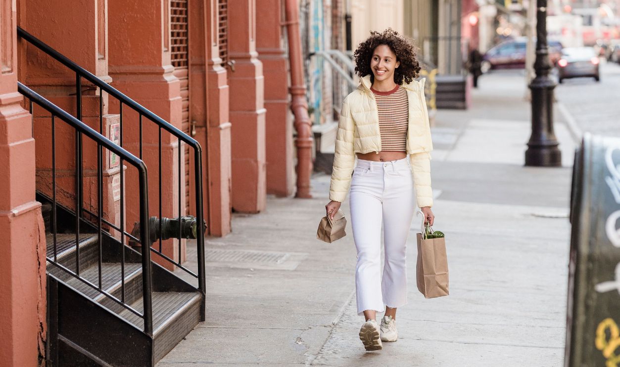 Cheerful woman walking on city street carrying paper bags, enjoying a casual urban stroll.