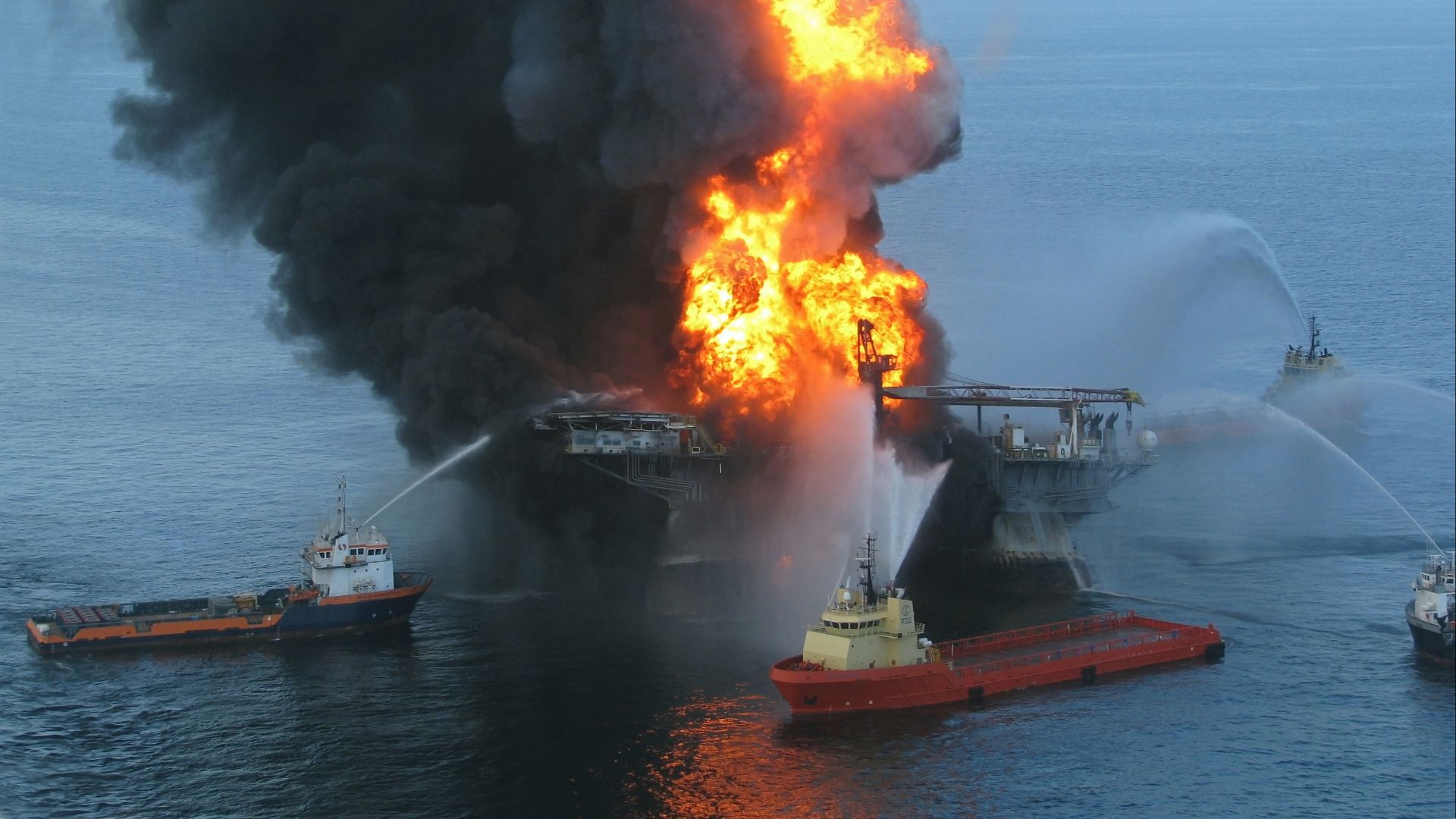 Platform supply vessels battle the blazing remnants of the off shore oil rig Deepwater Horizon. A Coast Guard MH-65C dolphin rescue helicopter and crew document the fire aboard the mobile offshore drilling unit Deepwater Horizon, while searching for survi