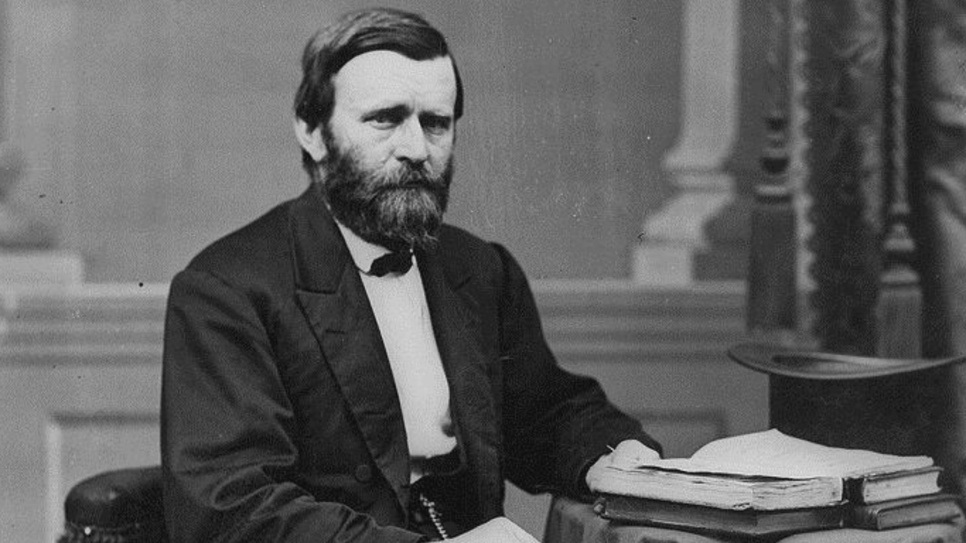 Ulysses S. Grant, full-length portrait, seated at table with books and top hat, facing right