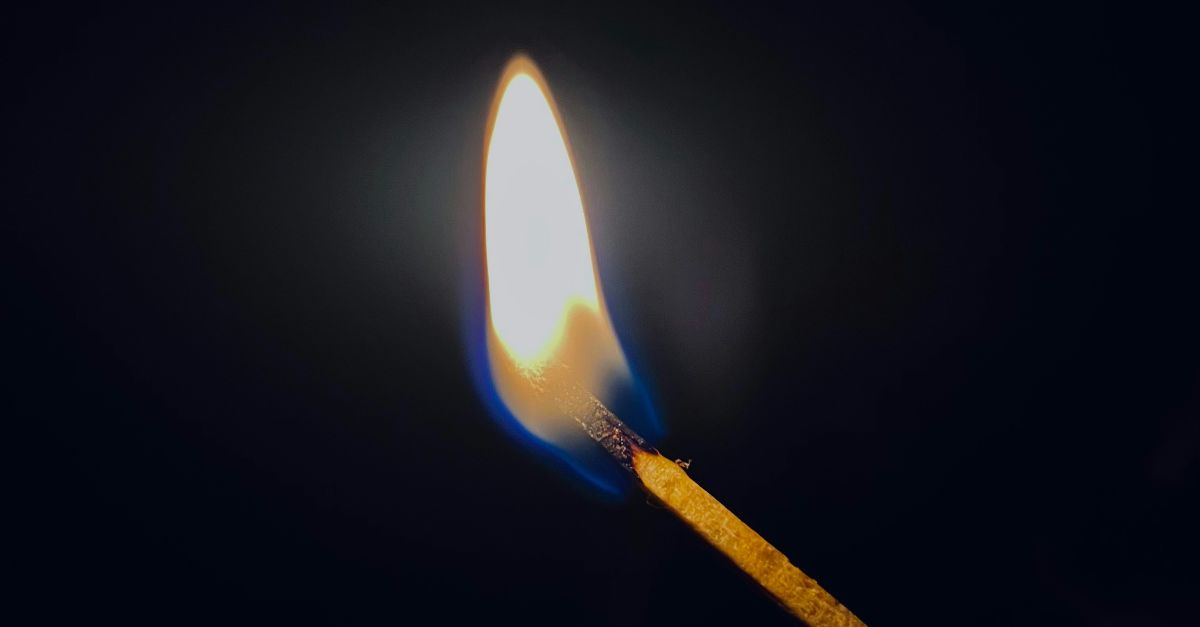 a lit matchstick in the dark with a lit match