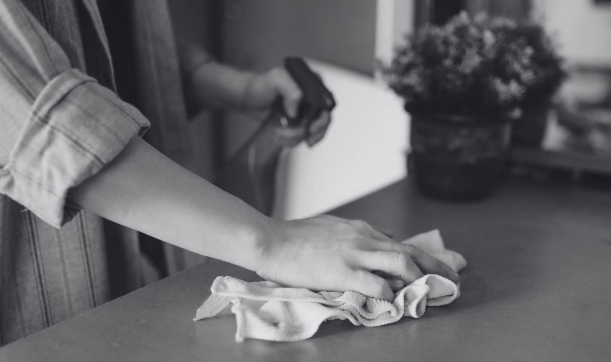 Close-up of a woman wiping a table with a spray bottle and cloth indoors, symbolizing effective housekeeping