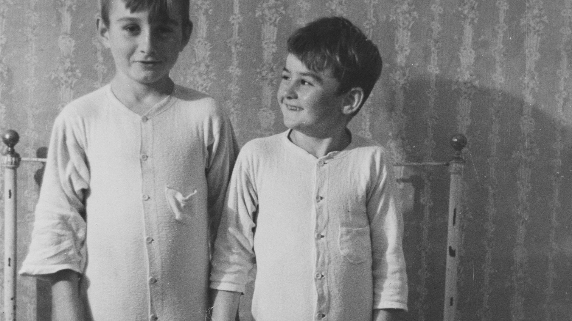Two boys in pajamas standing on a bed