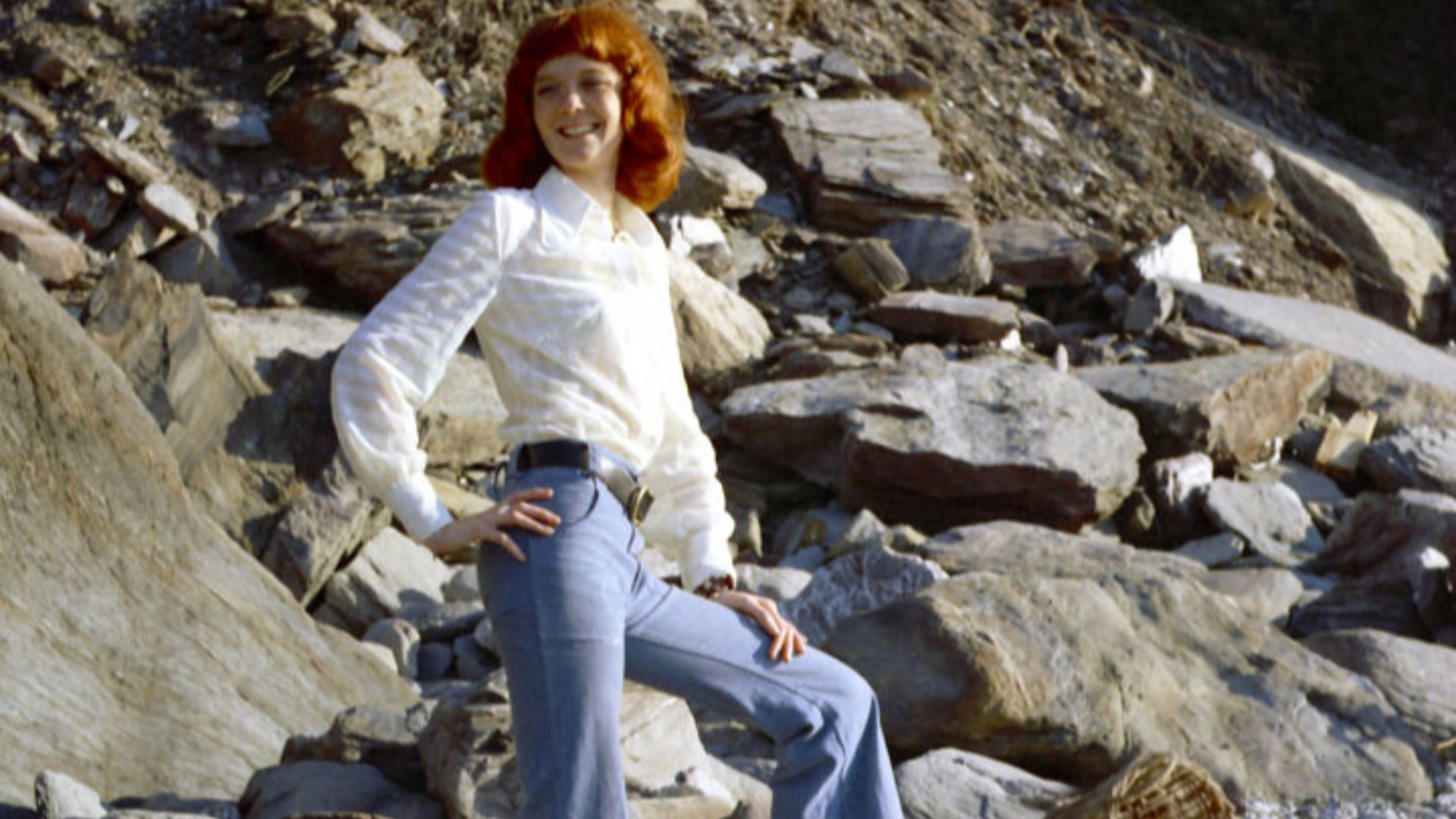 Tall natural redhead Erika on a North Devon beach in the UK, wearing bell bottom jeans. Mid 1970s.