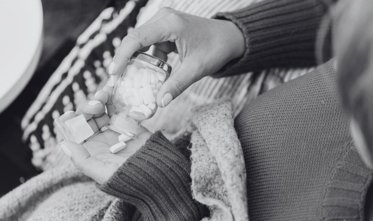 Close-up of a person holding a glass bottle with white pills, captured indoors