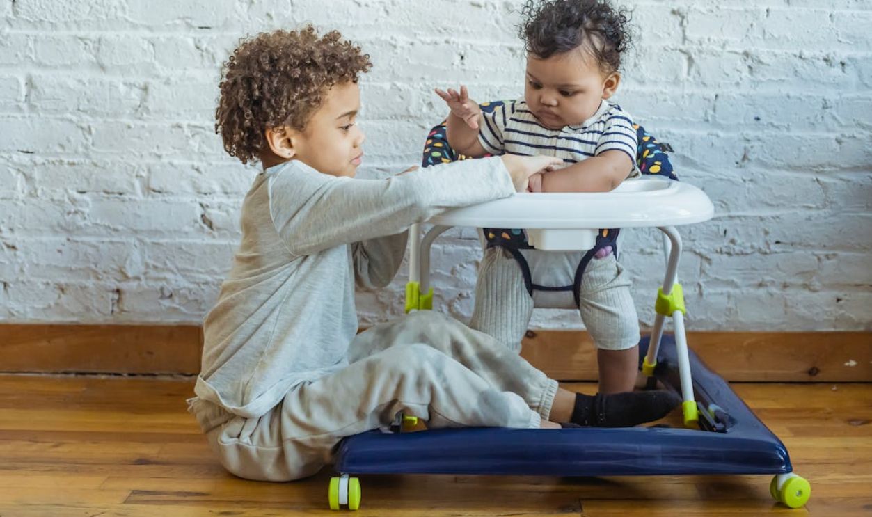 A young child and a toddler interacting playfully in a cozy home environment with a walker