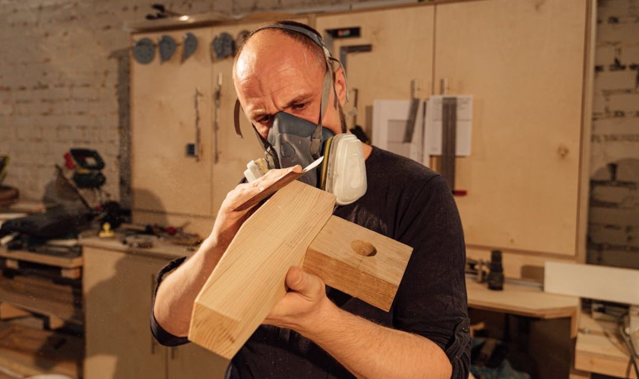 A focused carpenter uses hand tools to refine a wooden piece in an industrial workshop