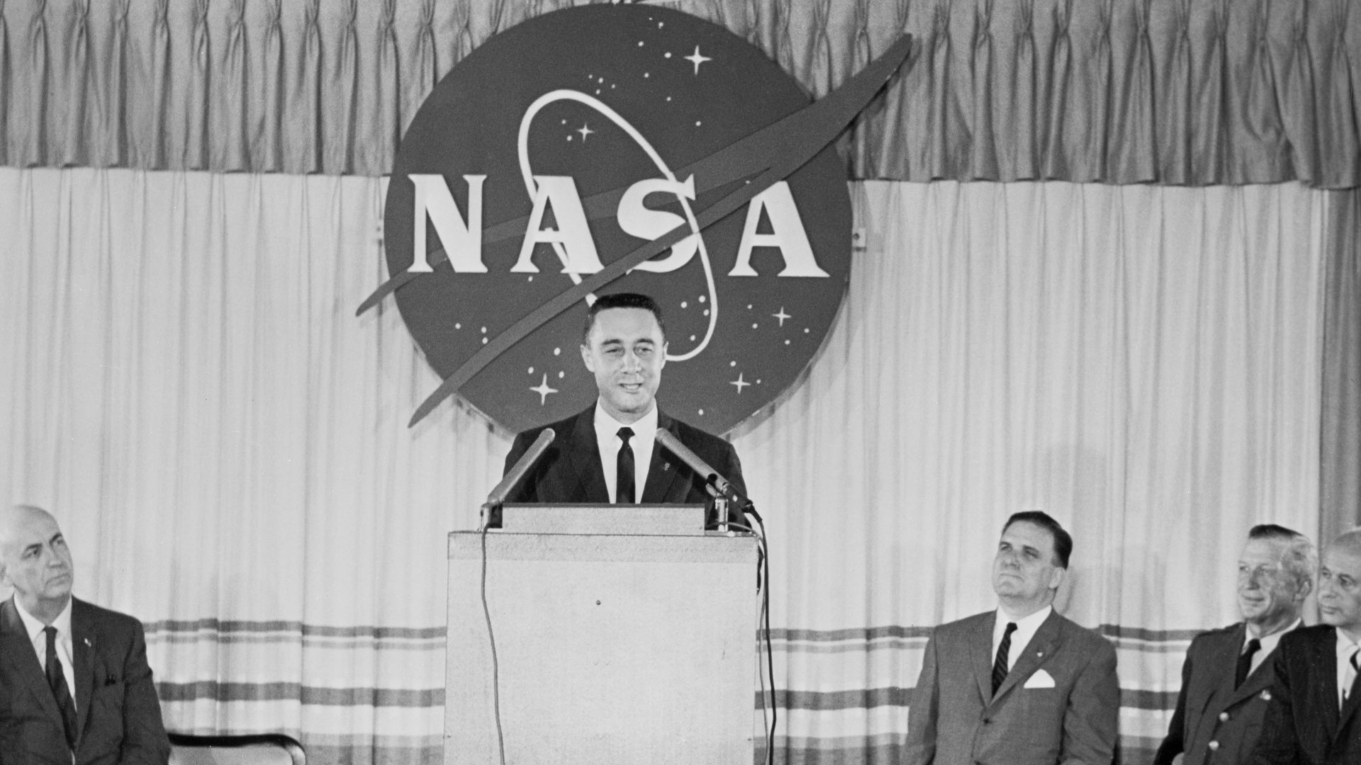 S61-03676 (23 July 1961) --- Astronaut Virgil I. (Gus) Grissom speaks at a press conference on July 23, 1961 held at the Starlight motel. Behind him is a large representation of the NASA logo. Photo credit: NASA
