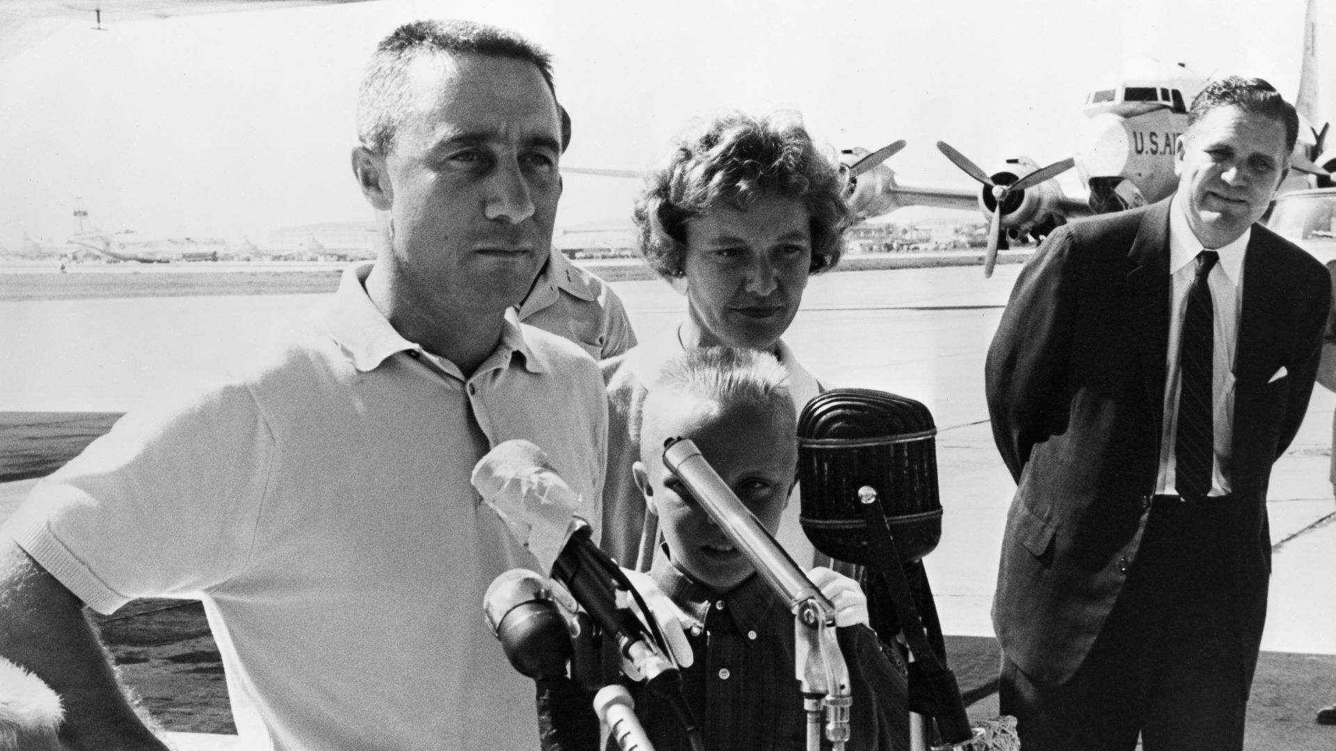 Astronaut Virgil I. (Gus) Grissom and his family are shown at the airport at Patrick Air Force Base with NASA Administrator James E. Webb (right). Grissom is speaking into microphones for the news media.