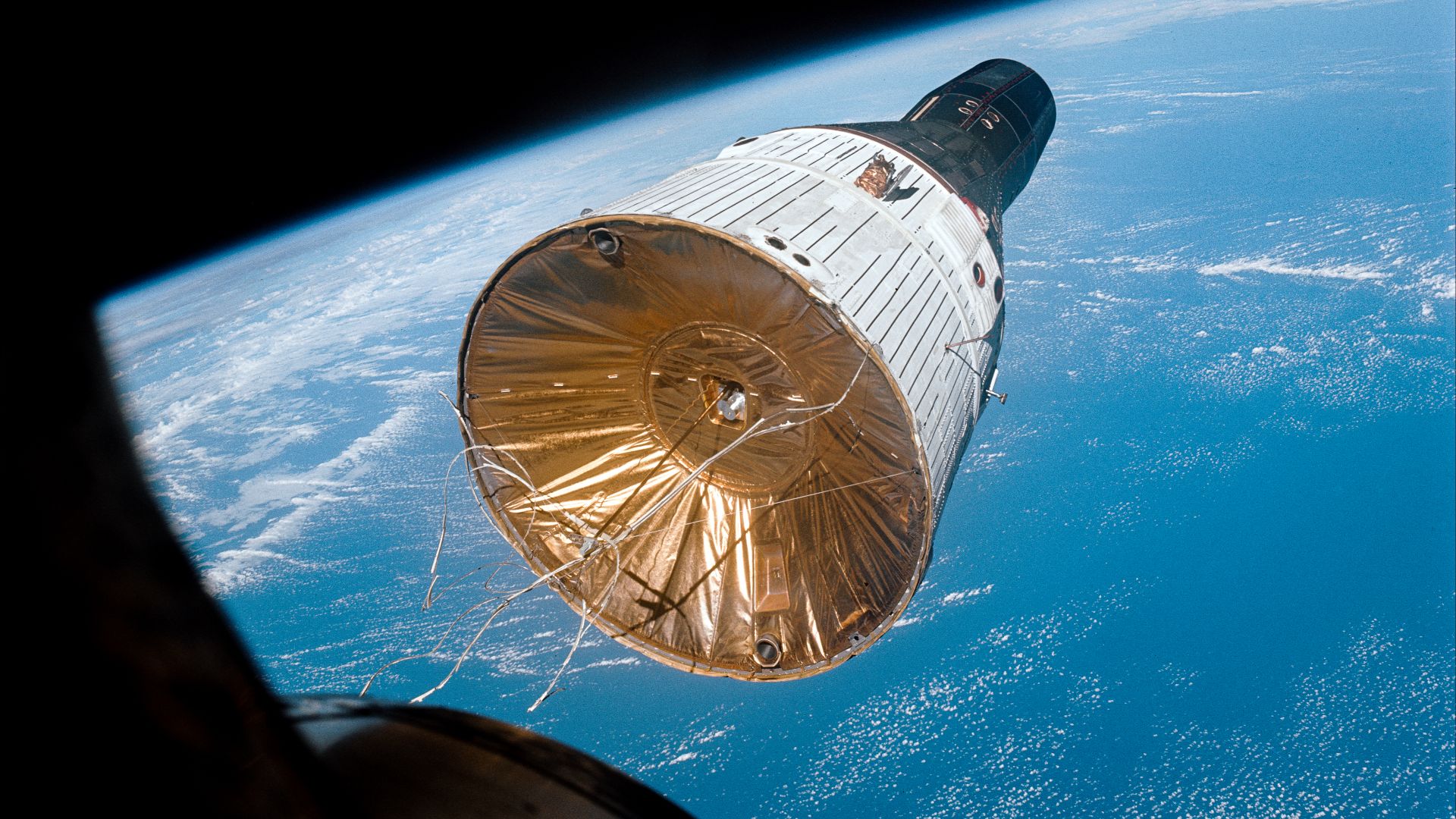 S65-63221 - This photograph of the Gemini-Titan 7 (GT-7) spacecraft was taken from the Gemini-Titan 6 (GT-6) spacecraft during the historic rendezvous of the two spacecraft on Dec. 15, 1965. The two spacecraft are some 37 feet apart here. Earth can be see