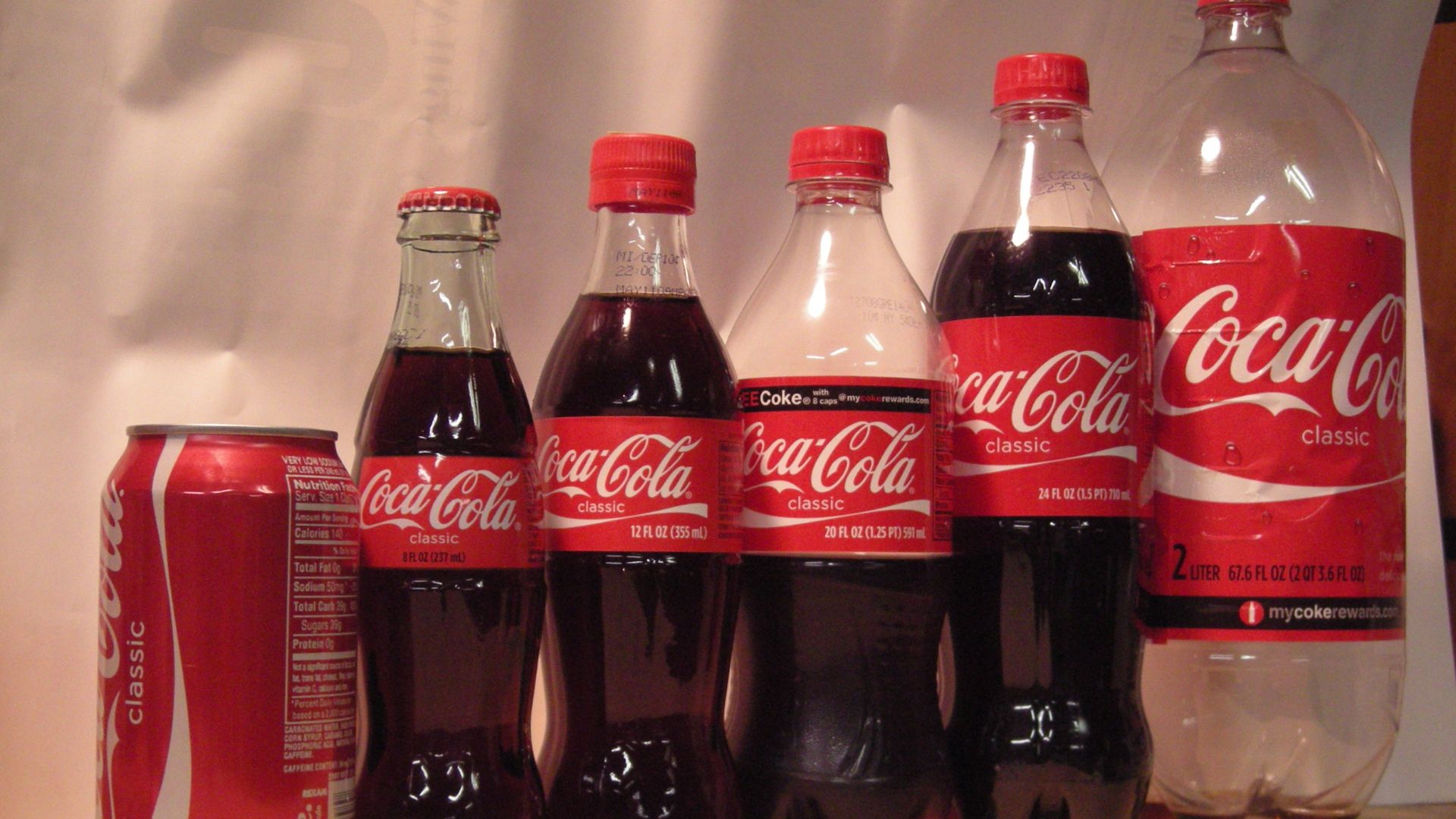 The various sizes of Coca-Cola available in the USA. Left to right: 12 oz can; 8 oz glass bottle; 12 oz resealable glass bottle; 20 oz, 24 oz and 2 Liter plastic bottles