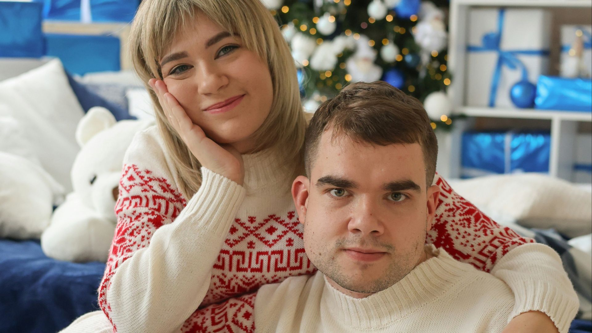 A man and woman sitting on a couch in front of a christmas tree