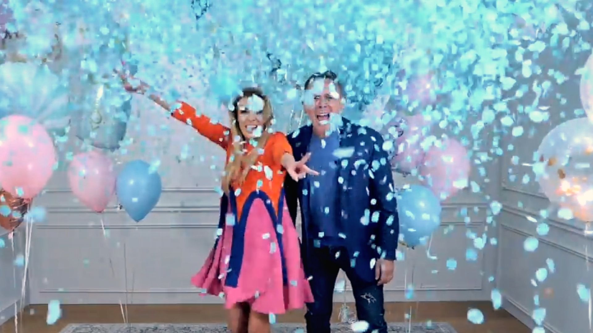 A couple celebrates a gender reveal with blue confetti suggesting a baby boy