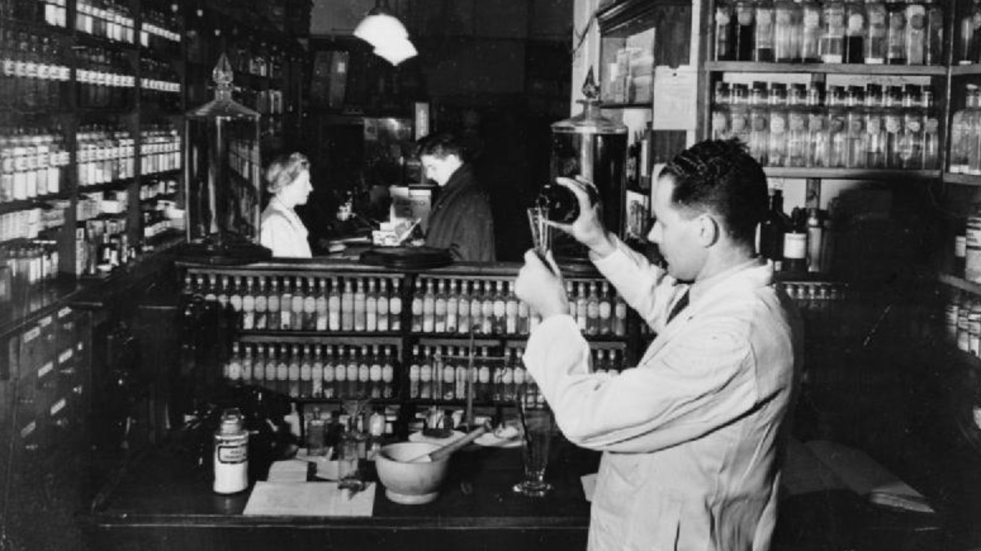 Turkish Opium For Britain- the USE of Opium in British Medicine, UK, 1943
A scene in a retail chemist's shop, showing the chemist making up a doctor's prescription from galenicals received from a manufacturing chemist.  Galenicals are concentrated extract