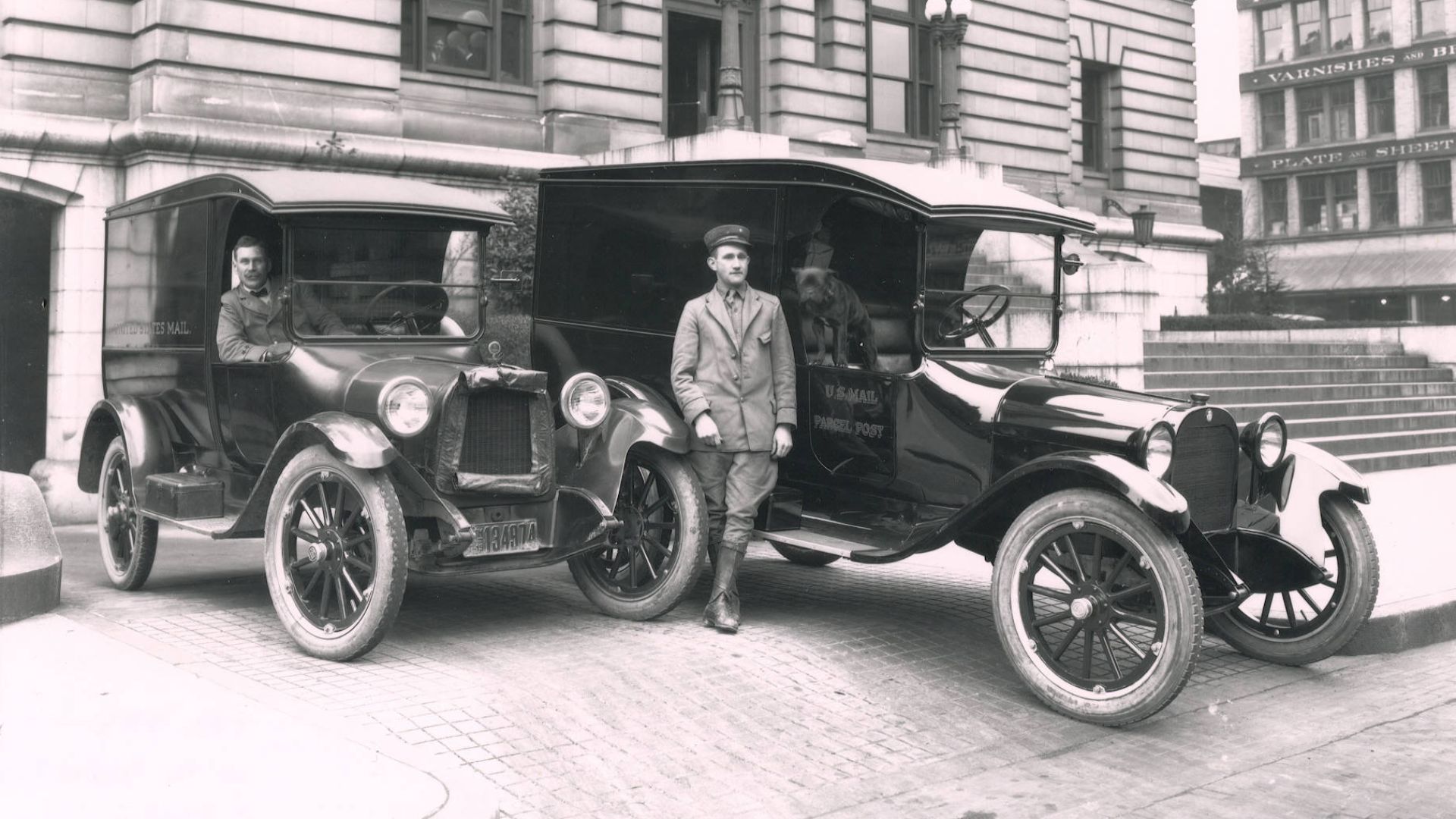 In April of 1919, two postal carriers, S.P. Hammerbeck and Charlie Matters (order not known), and their trusty dog posed with their shining black delivery vehicles on the brick areas outside the Federal Building at 1102 A Street, in downtown Tacoma. The U