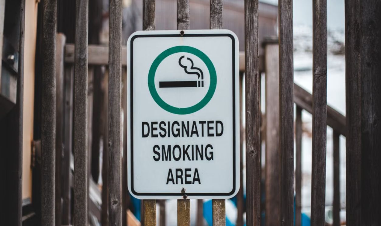 Sign indicating designated smoking area with wooden fence backdrop, emphasizing legal smoking zones.