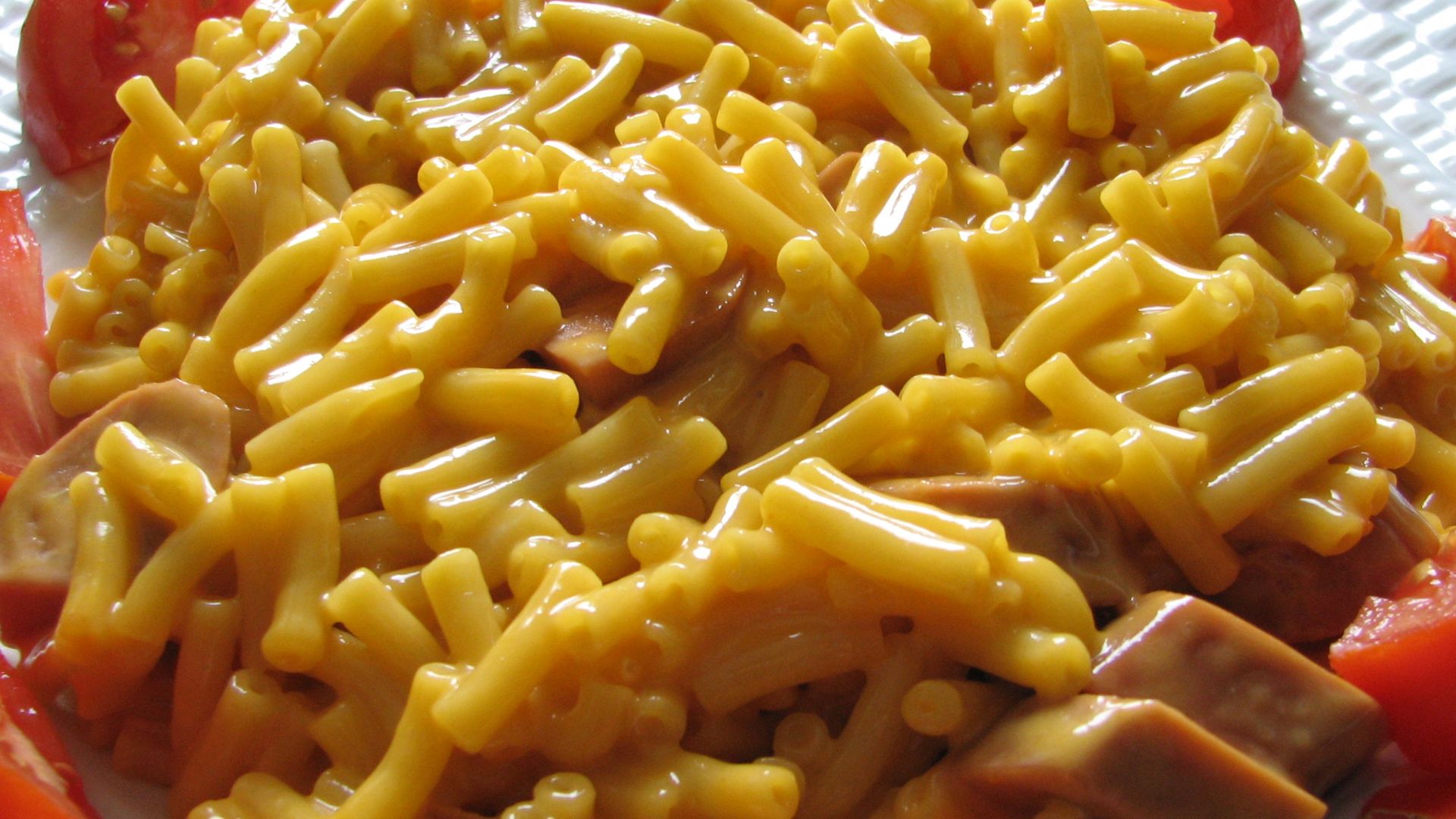 Kraft Dinner (macaroni and cheese) with added cheddar and sliced vegetarian hot dogs arranged on a plate and bordered by tomato wedges.  Photographer's comment: