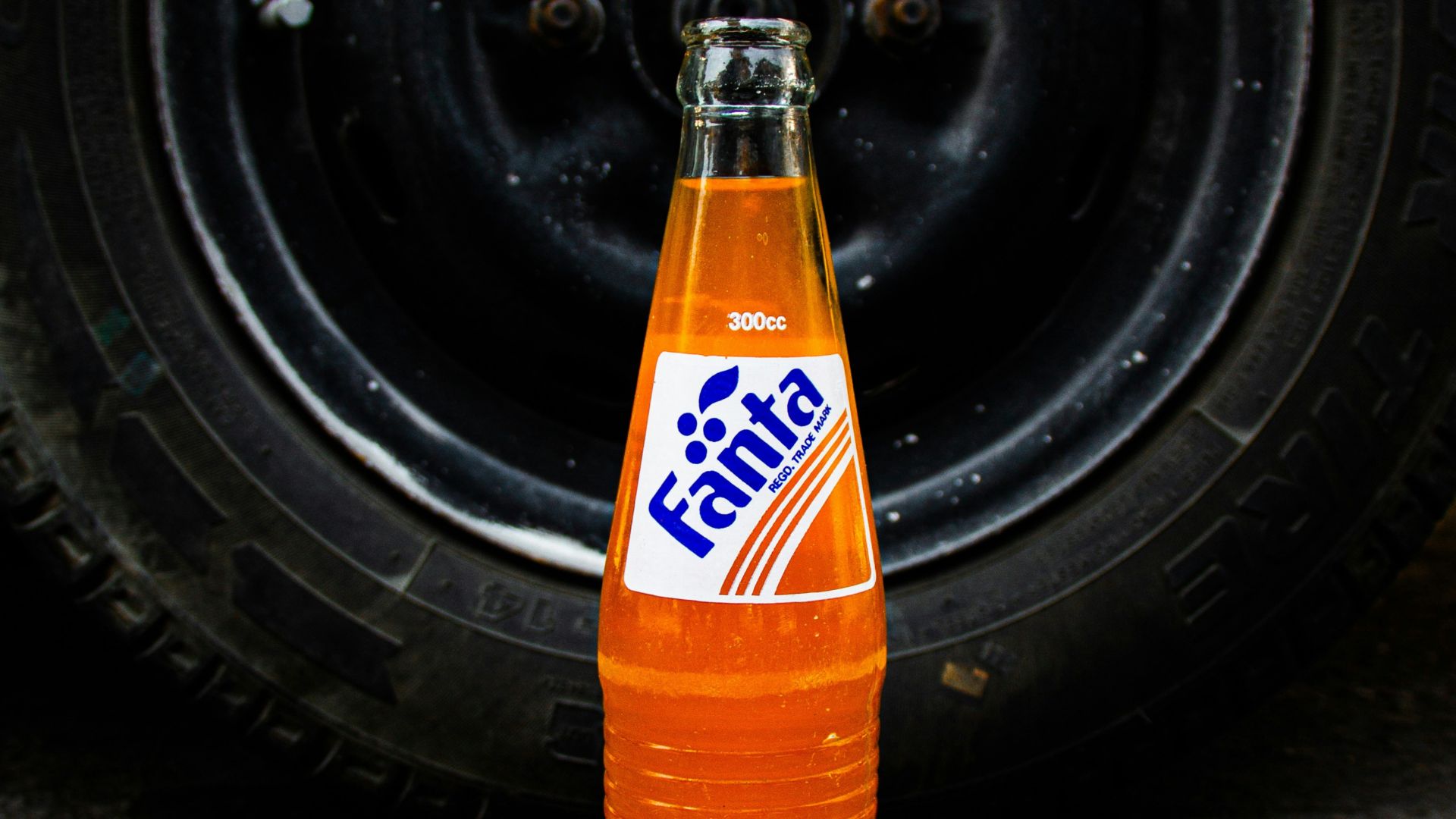 a bottle of soda sitting on the ground next to a tire