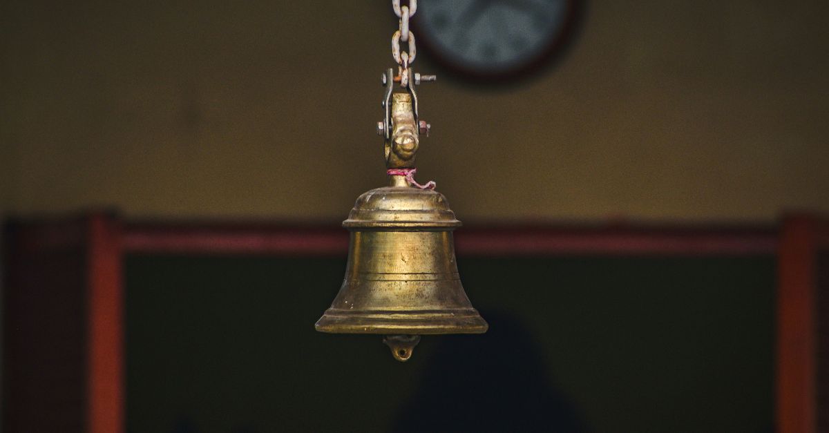 a bell hanging from a chain in front of a clock