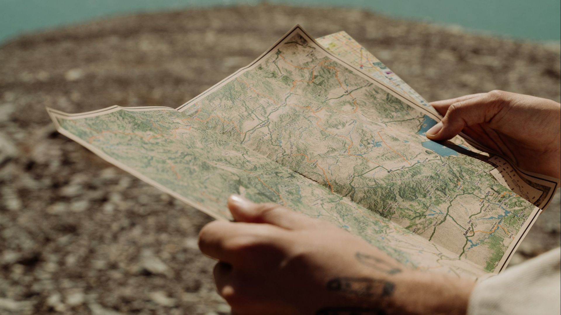 Hands holding a map by a tranquil lake, symbolizing exploration and adventure.