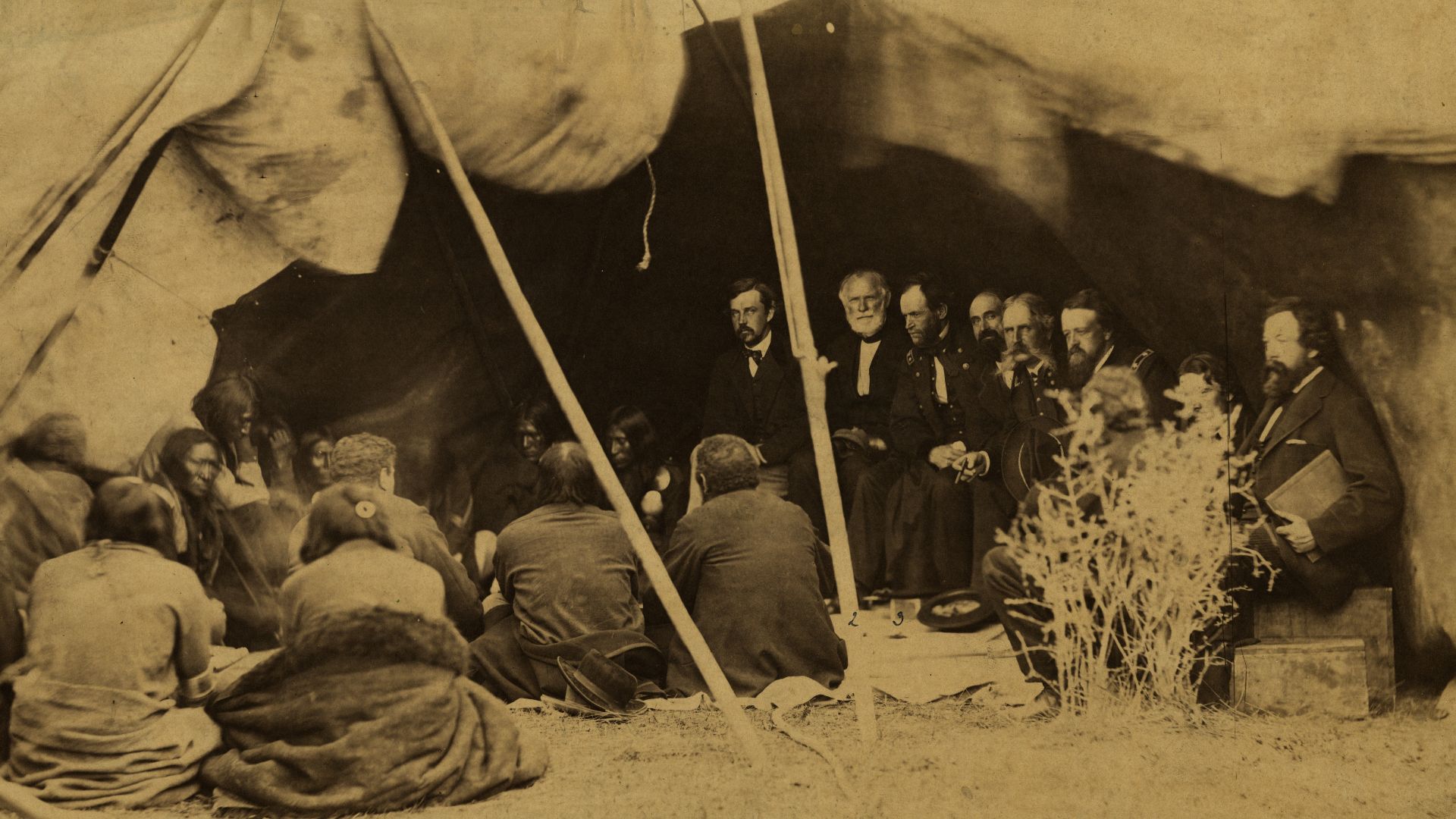 Group of American Indians and United States Army Commissioners in tent structure with wide, staked-up opening; Indians sit on ground at left, and Commissioners at right on boxes.  General William S. Harney and General William T. Sherman are among the Comm