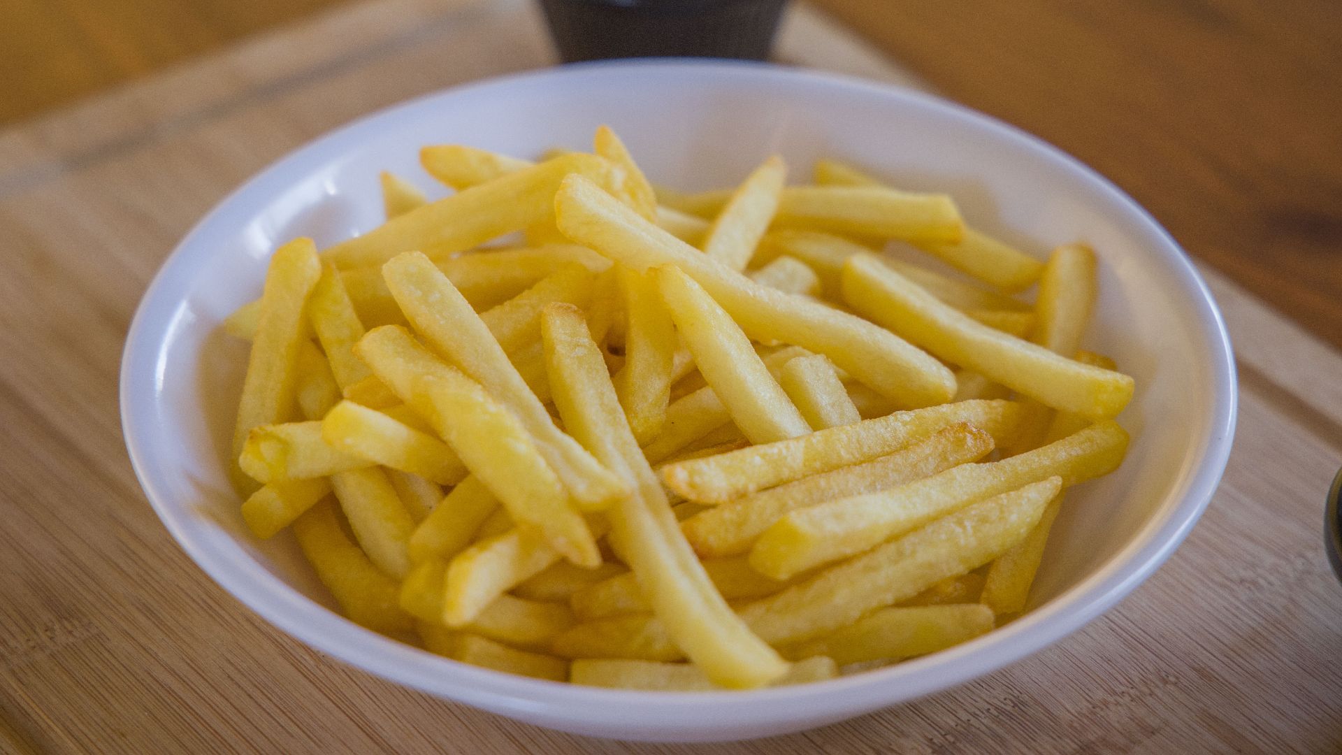 Crispy golden french fries served in a white ceramic bowl on a wooden table.