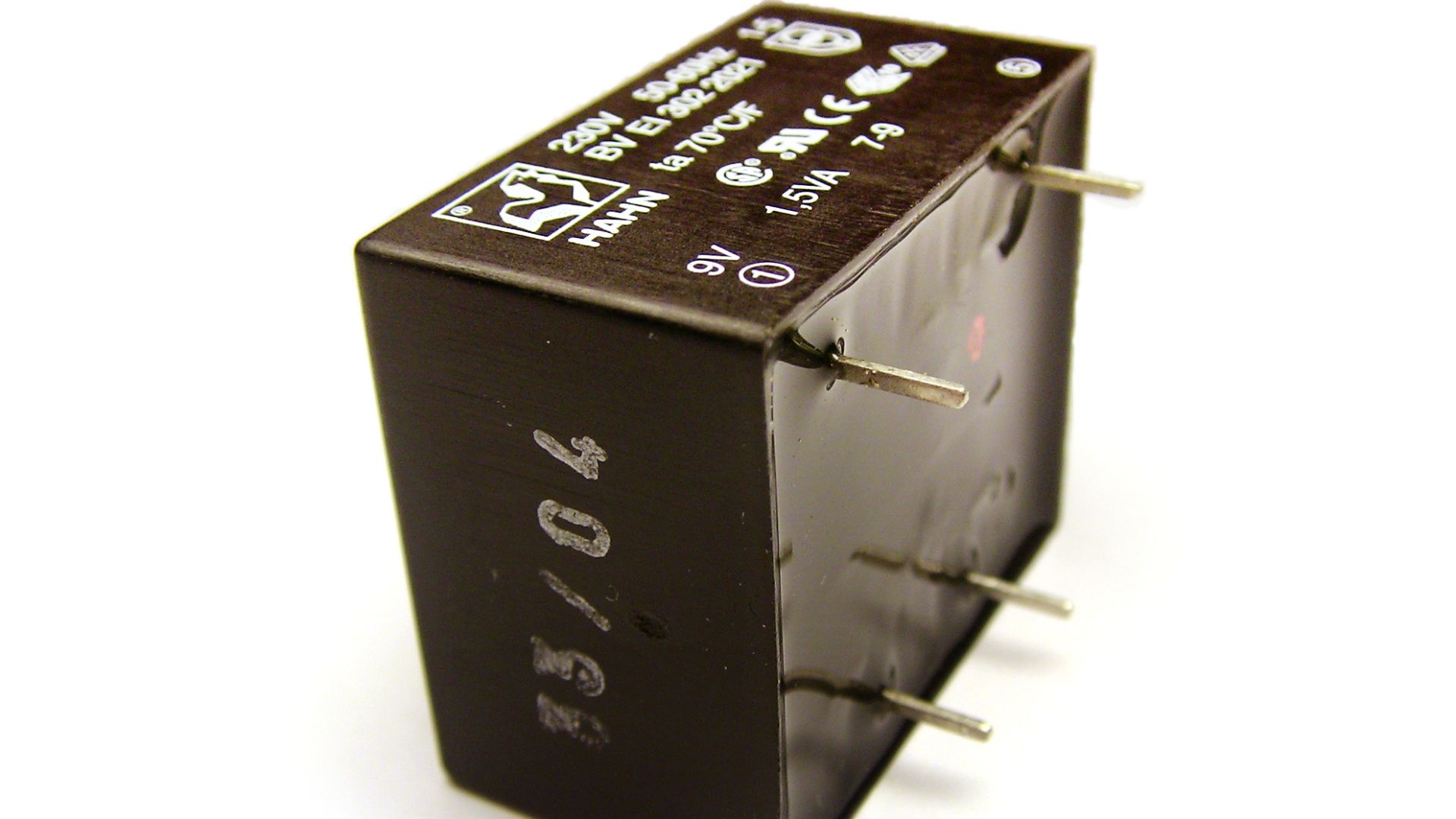 A small potted electrical transformer that is designed to be installed on a PCB. The surface formed by the potting compound (probably epoxy) is visible on the right. Other sides are formed by the plastic potting box.