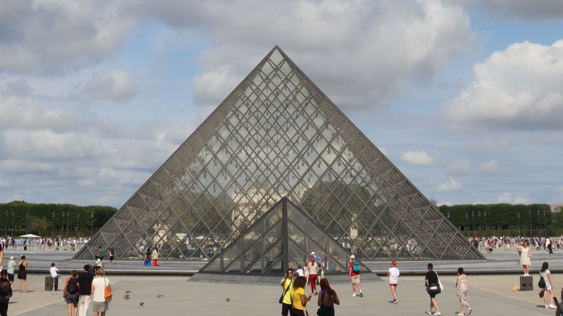 View of the Louvre Pyramid under a vibrant blue sky in Paris, France.