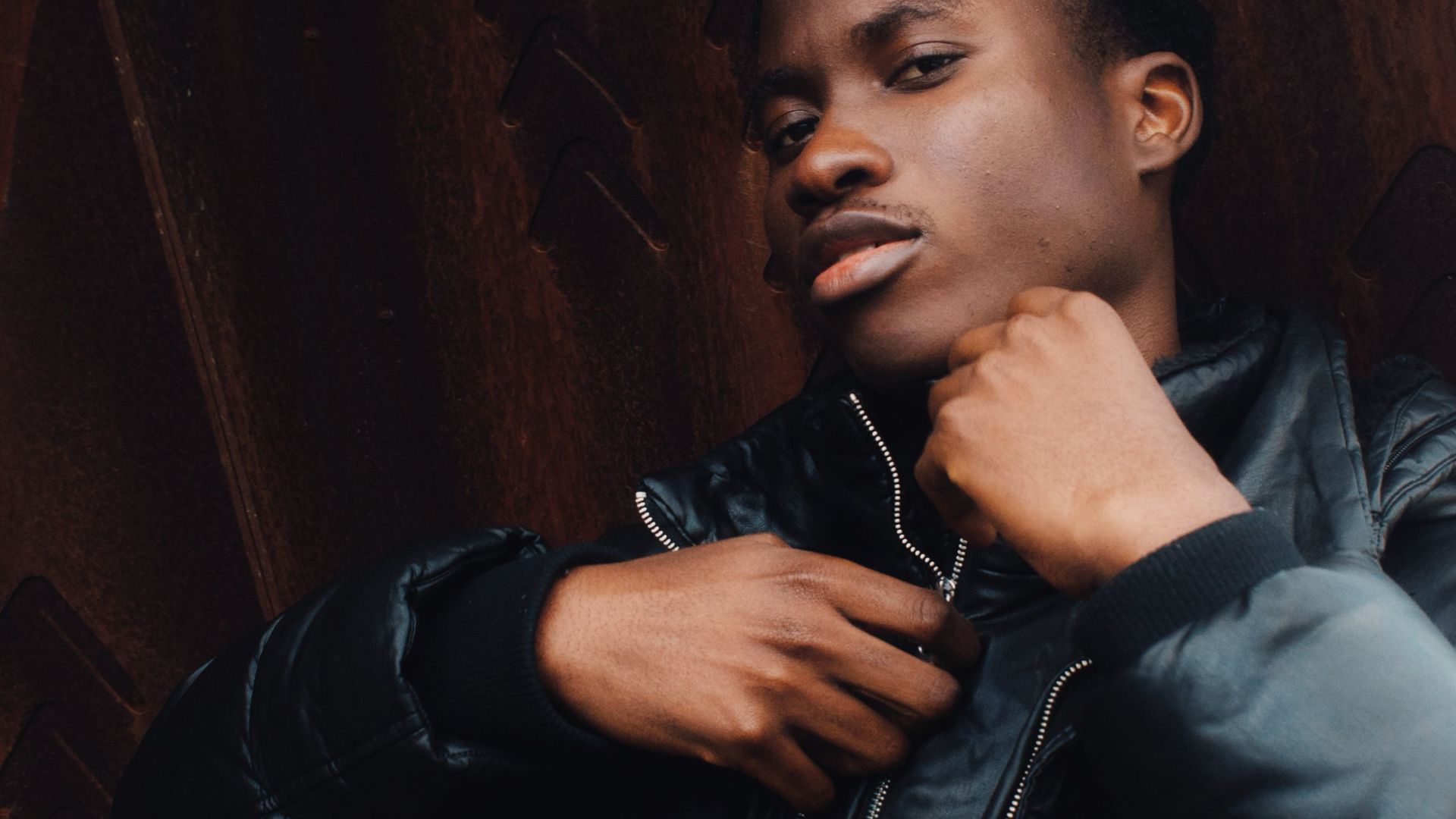 Urban portrait of a man in a black jacket posing confidently outdoors.