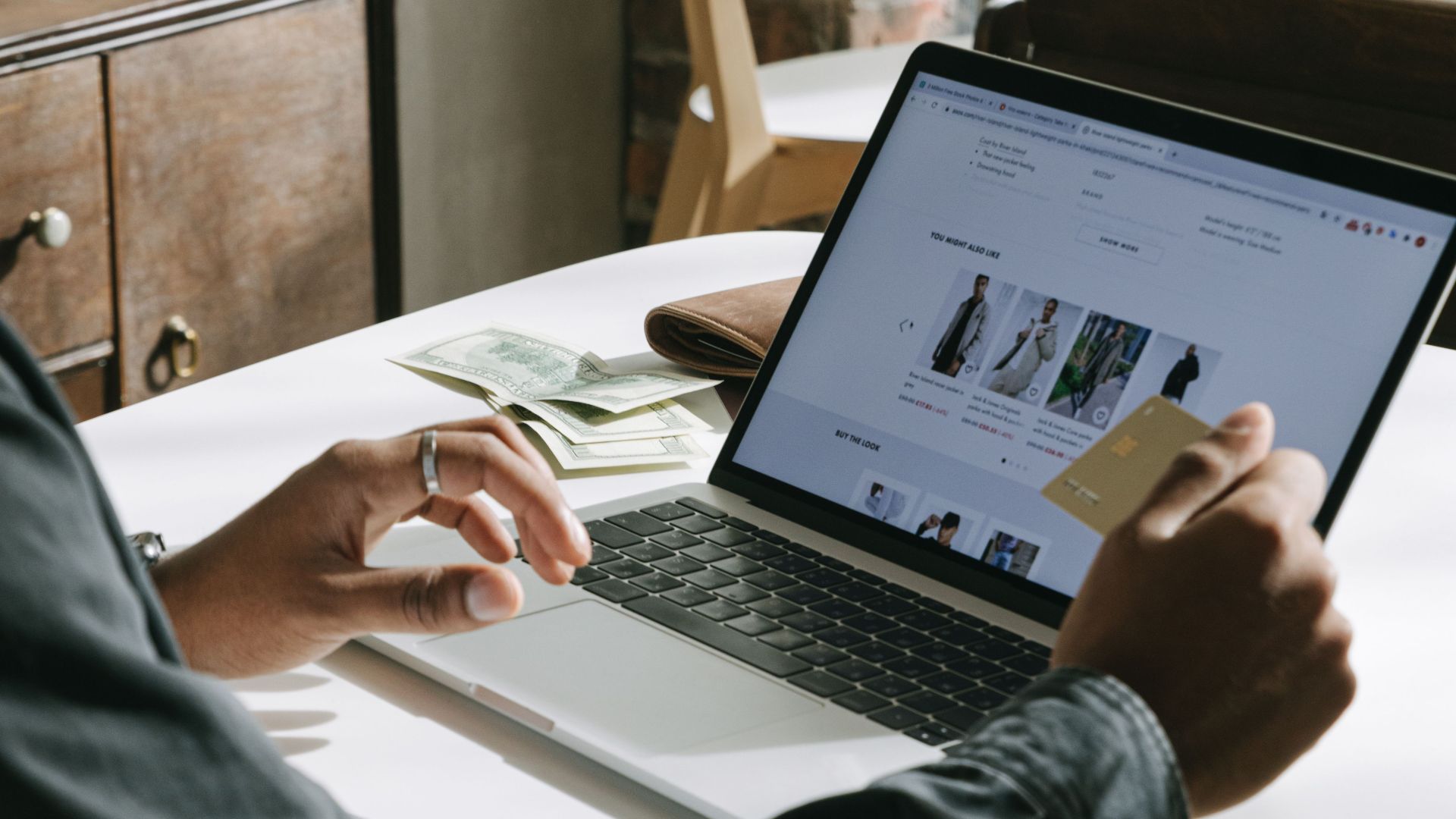 An adult uses a credit card for online shopping on a laptop indoors.