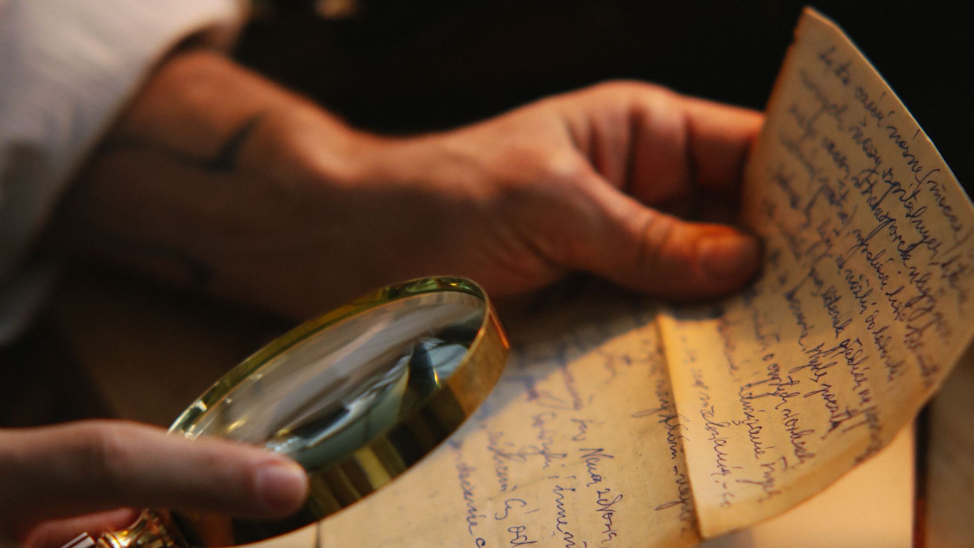 Close-up of a person inspecting a vintage handwritten letter with a magnifying glass.