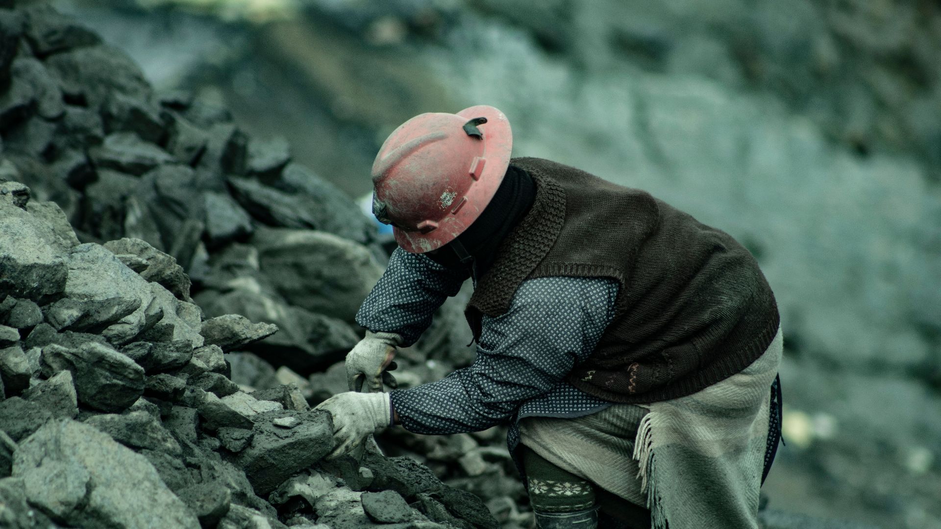 A coal miner in a hard hat working amidst rocky terrain, emphasizing labor and resilience.
