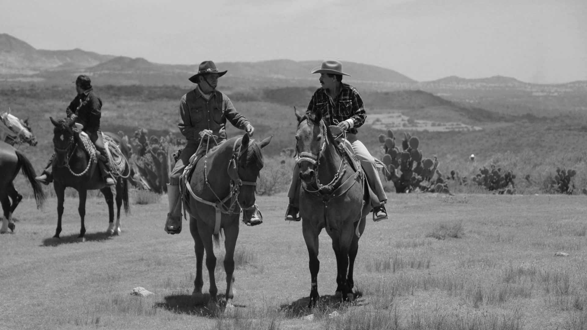 Black and white photo of cowboys riding horses through a scenic desert landscape.