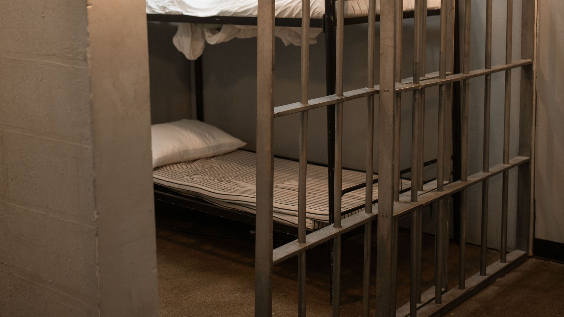 A prison cell featuring a metal bunk bed and striped sheets.