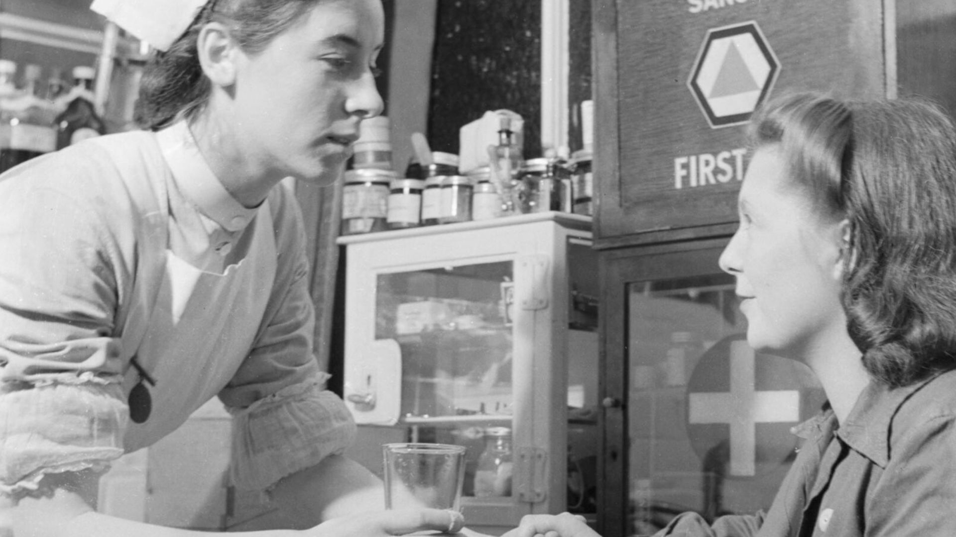 Pregnat wartime worker Irene Stacey visits the nurse in a clinic attached to the factory where she works in Bristol, 1942.
Irene Stacey speaks to the factory nurse, who gives her a glass of water, in the clinic attached to the factory where she works in B