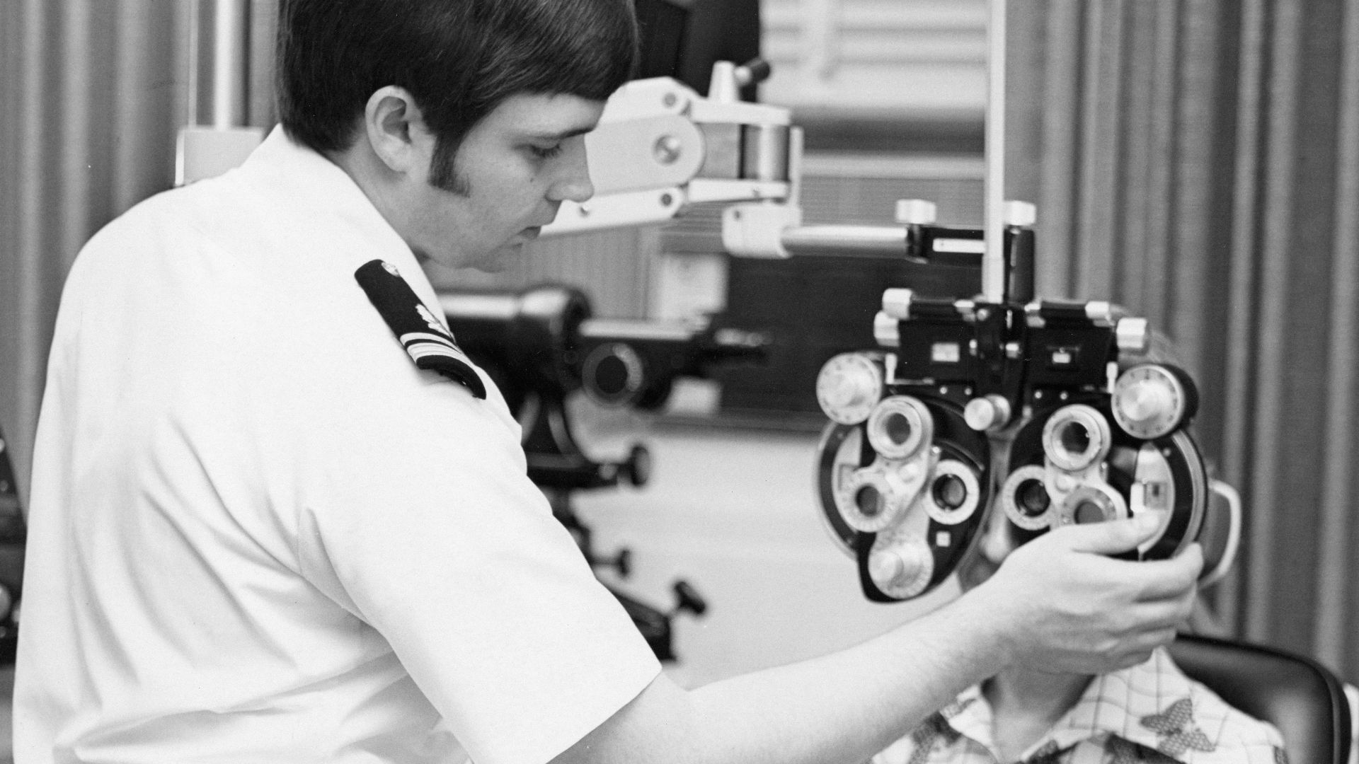 An optometrist examines a patient's eyes with a phoropter.