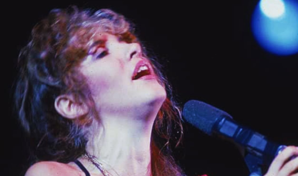 American pop and rock singer Stevie Nicks (of the group Fleetwood Mac) sings into a microphone onstage as she holds a rose against her chest, early 1990s.