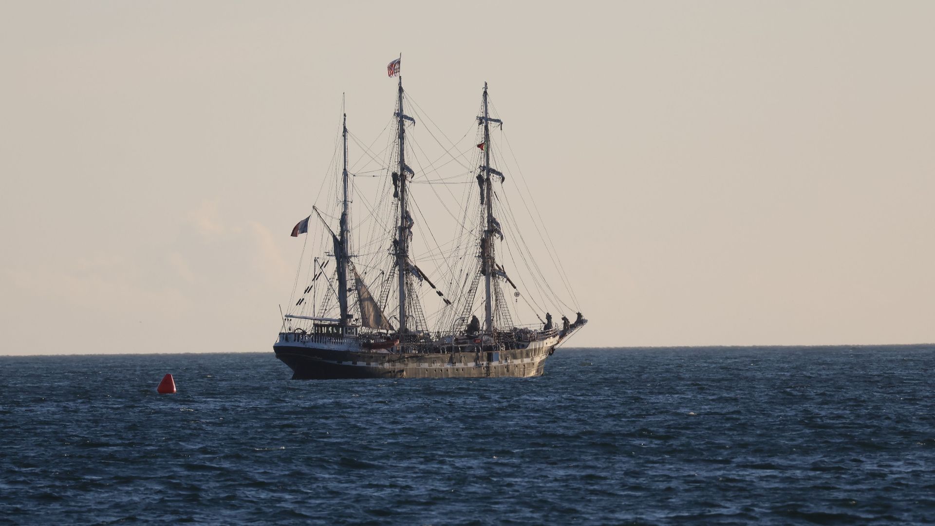 A classic tall ship sails majestically across the open sea under a serene sky at dusk.