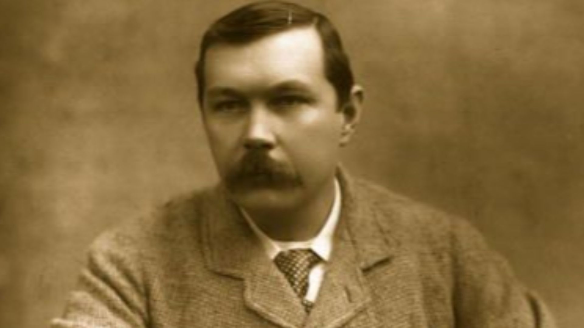 Photograph of Arthur Conan Doyle, seated sideways on chair. Published in