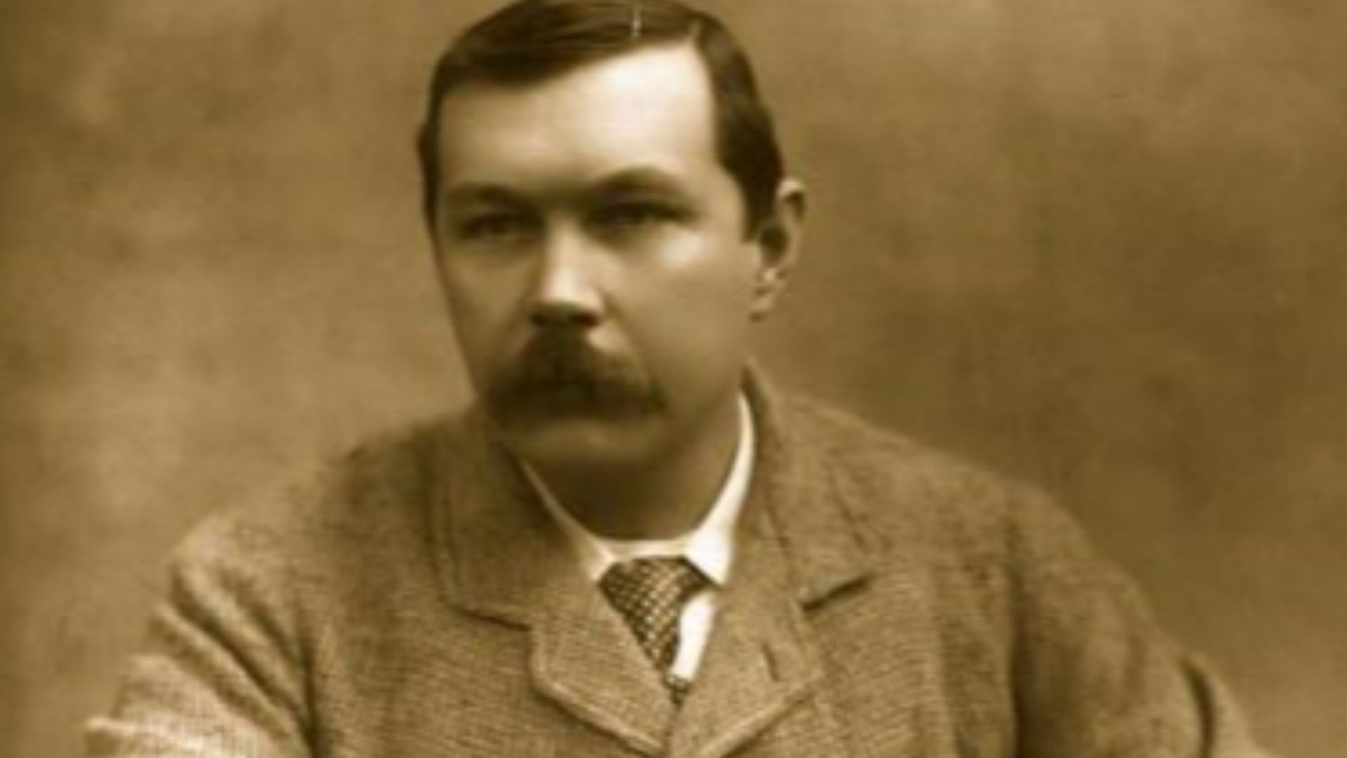 Photograph of Arthur Conan Doyle, seated sideways on chair. Published in