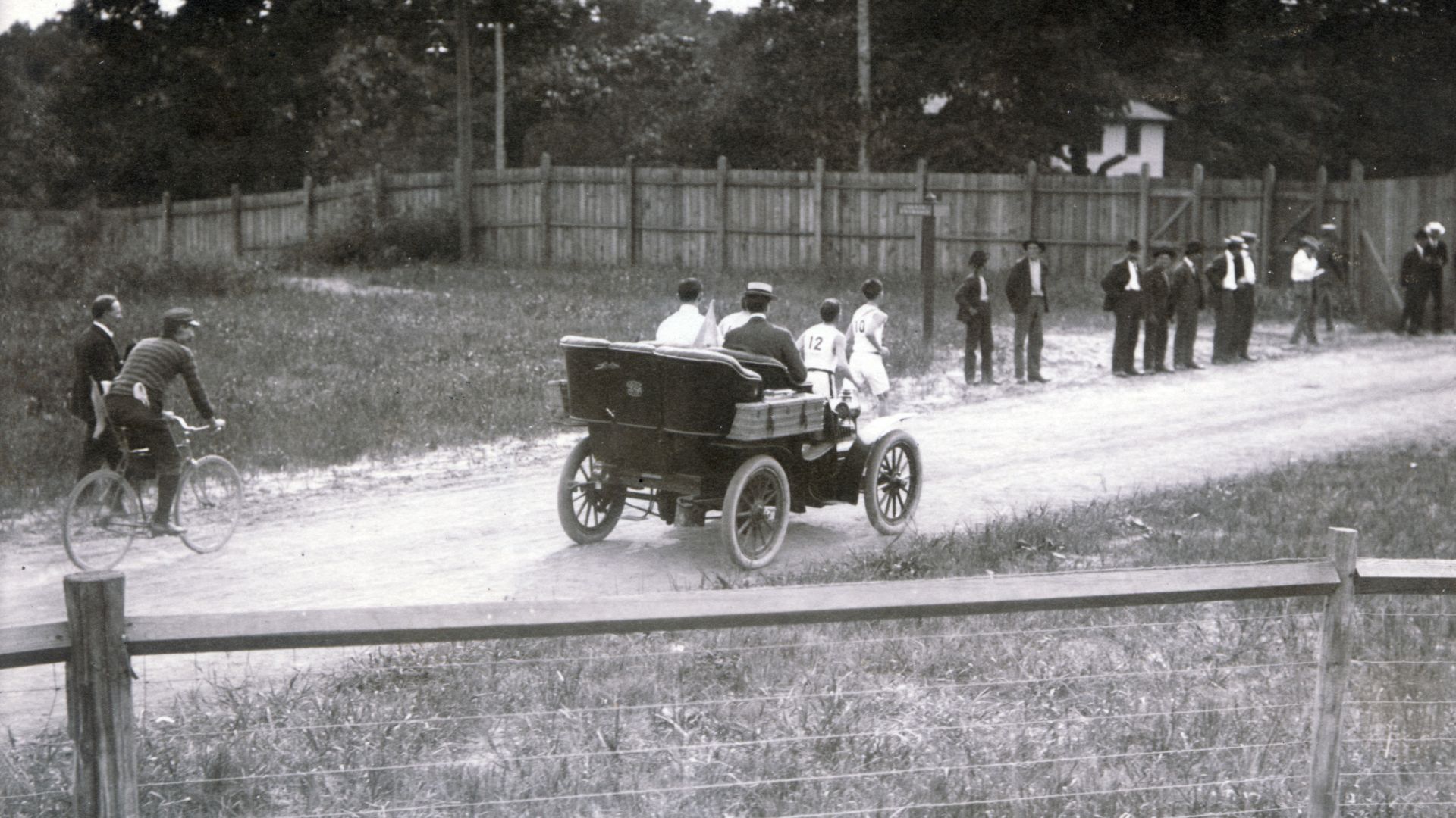 First participants out of stadium, Samuel Mellor and Michael Spring, in front of referees' auto mobile with scatterd crowd watching.Title: First runners leaving the stadium during the 1904 Olympic Marathon Race. (Mellor and Spring in front of referees' au