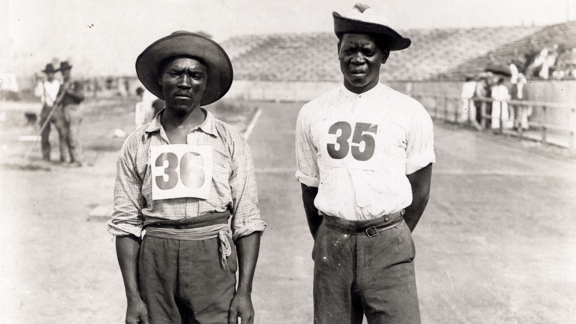 Jan Mashiani (#36, left) and Len Taunyane (#35, right) of the Tswana tribe (though billed as Zulus)[1] of South Africa facing camera standing on the track. Taunyane finished the marathon in ninth place, while Mashiani came in twelfth. Legend has it that o