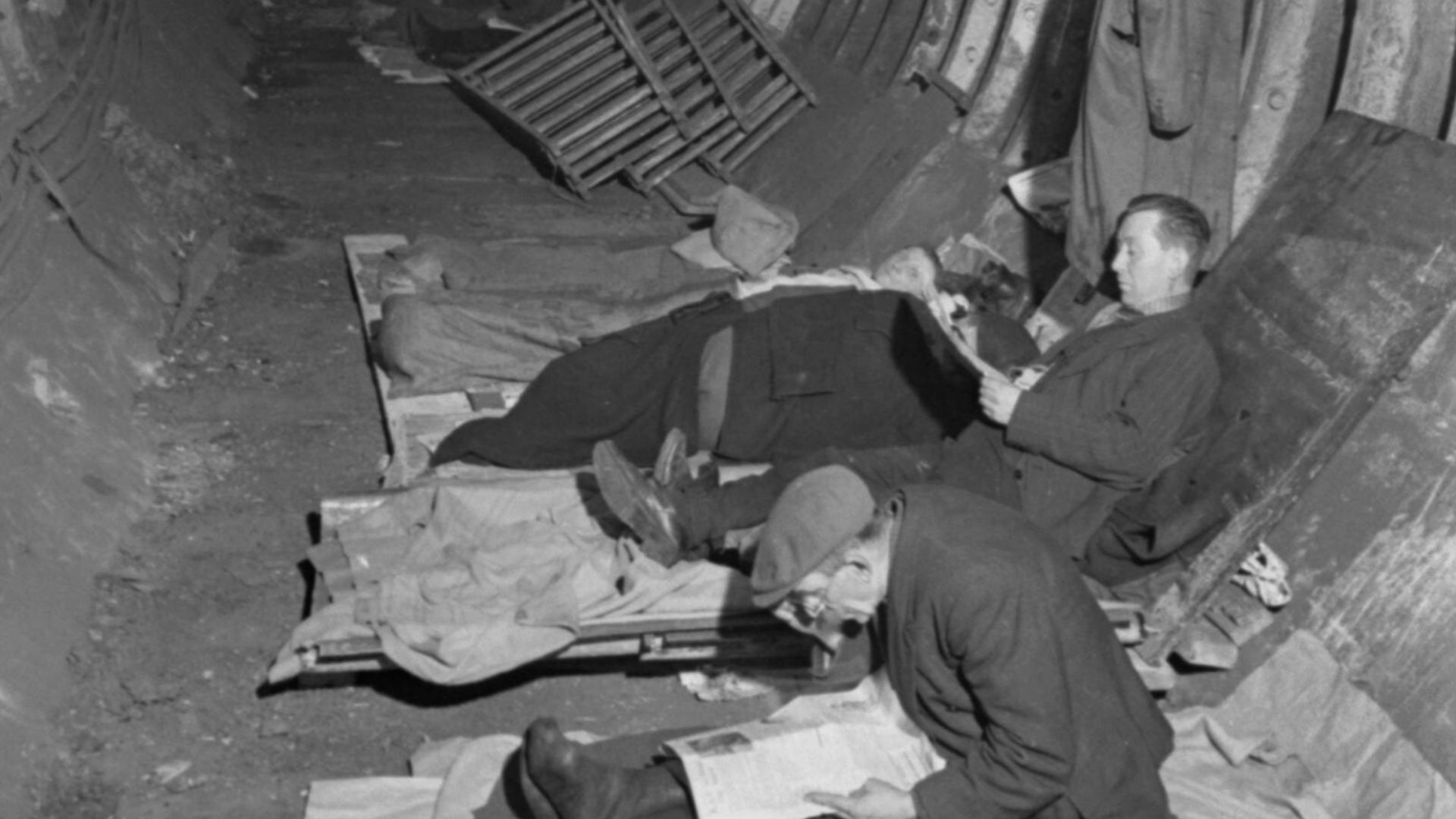 Londoners spending the night in a tunnel of the London Underground network, probably at Aldwych, in November 1940.
Shelterers read the paper and prepare for sleep in a dimly-lit tunnel of the London Underground network, probably at Aldwych in November 194