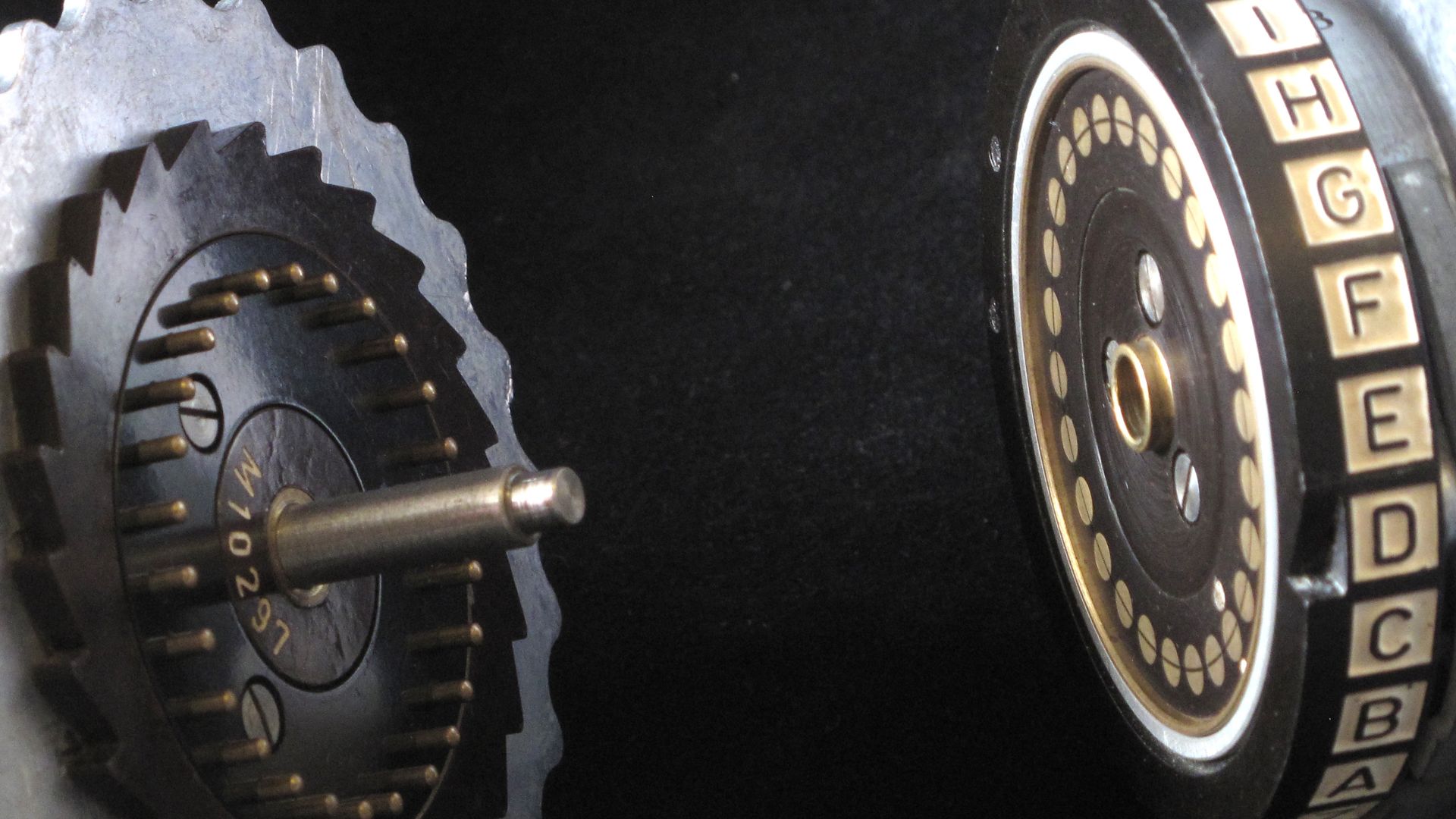 Two Enigma rotors and the spindle on which they are mounted. When the machine is assembled, the spring-loaded studs on the right hand side of rotor (pictured left), make electrical contact with the brass contacts on the left hand side of the rotor (pictur