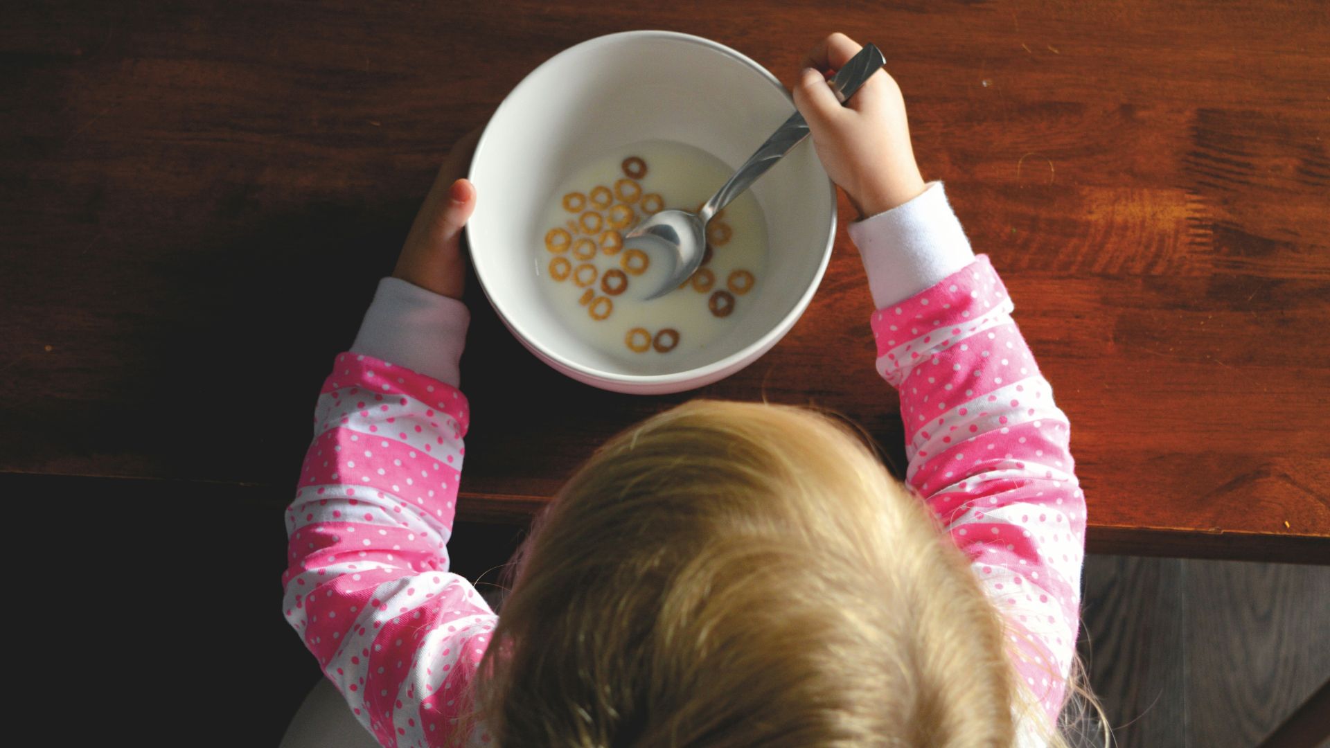 girl eating cereal in white ceramic bowl on table
