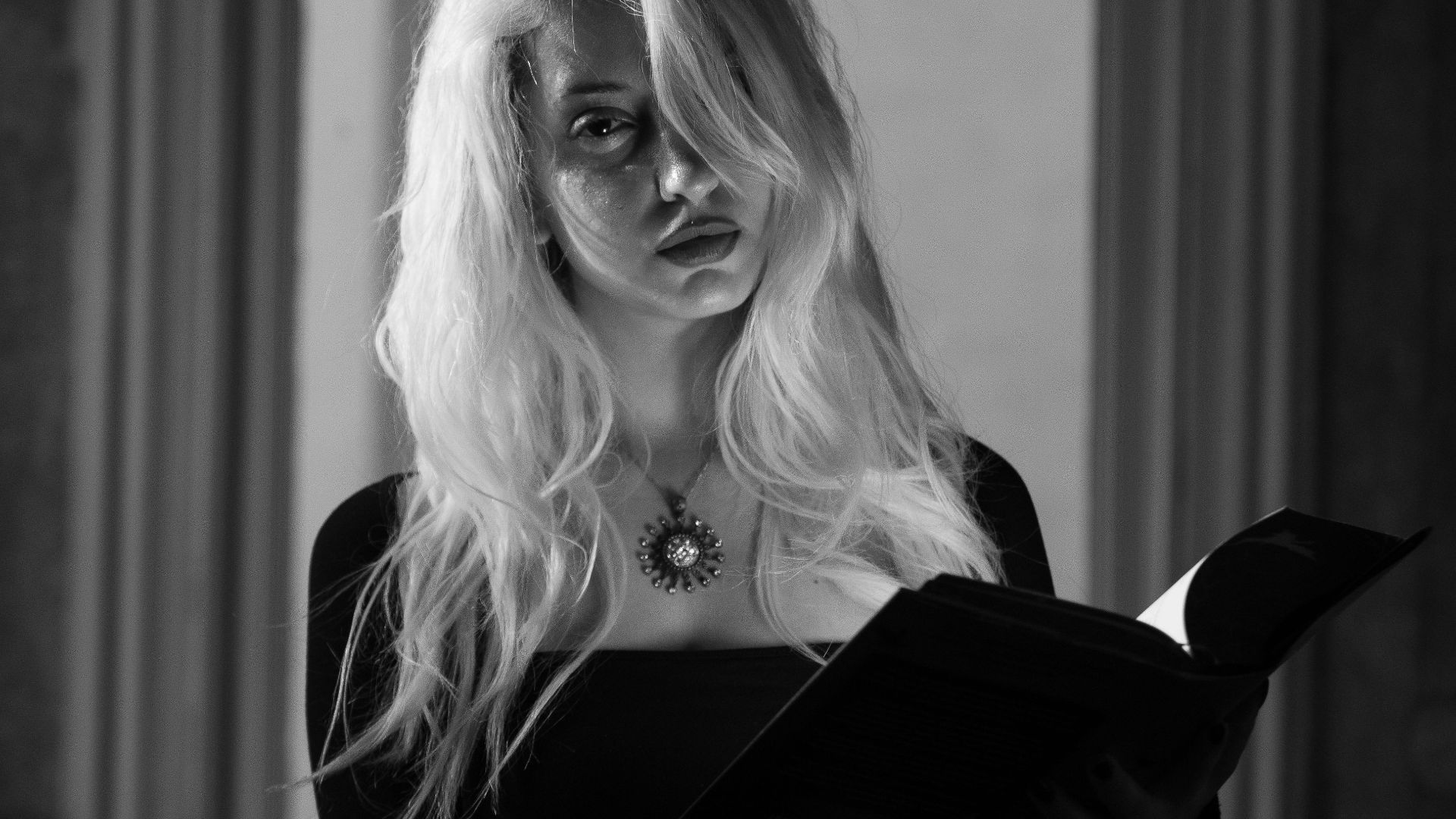 Black and white portrait of a woman reading under a chandelier, exuding elegance and mystery.