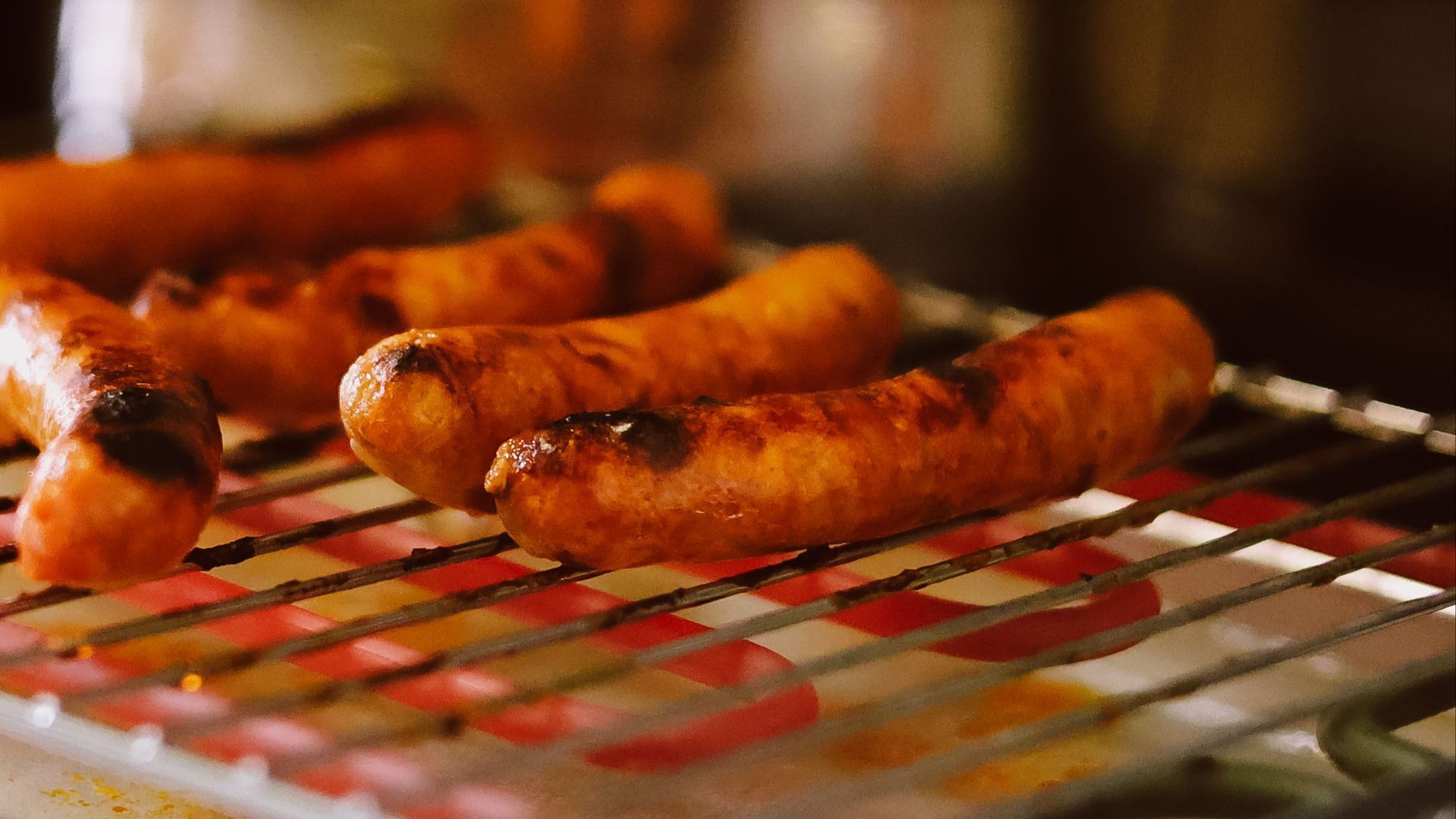 Close-up of grilled sausages on a kitchen grill with a pot in the background.