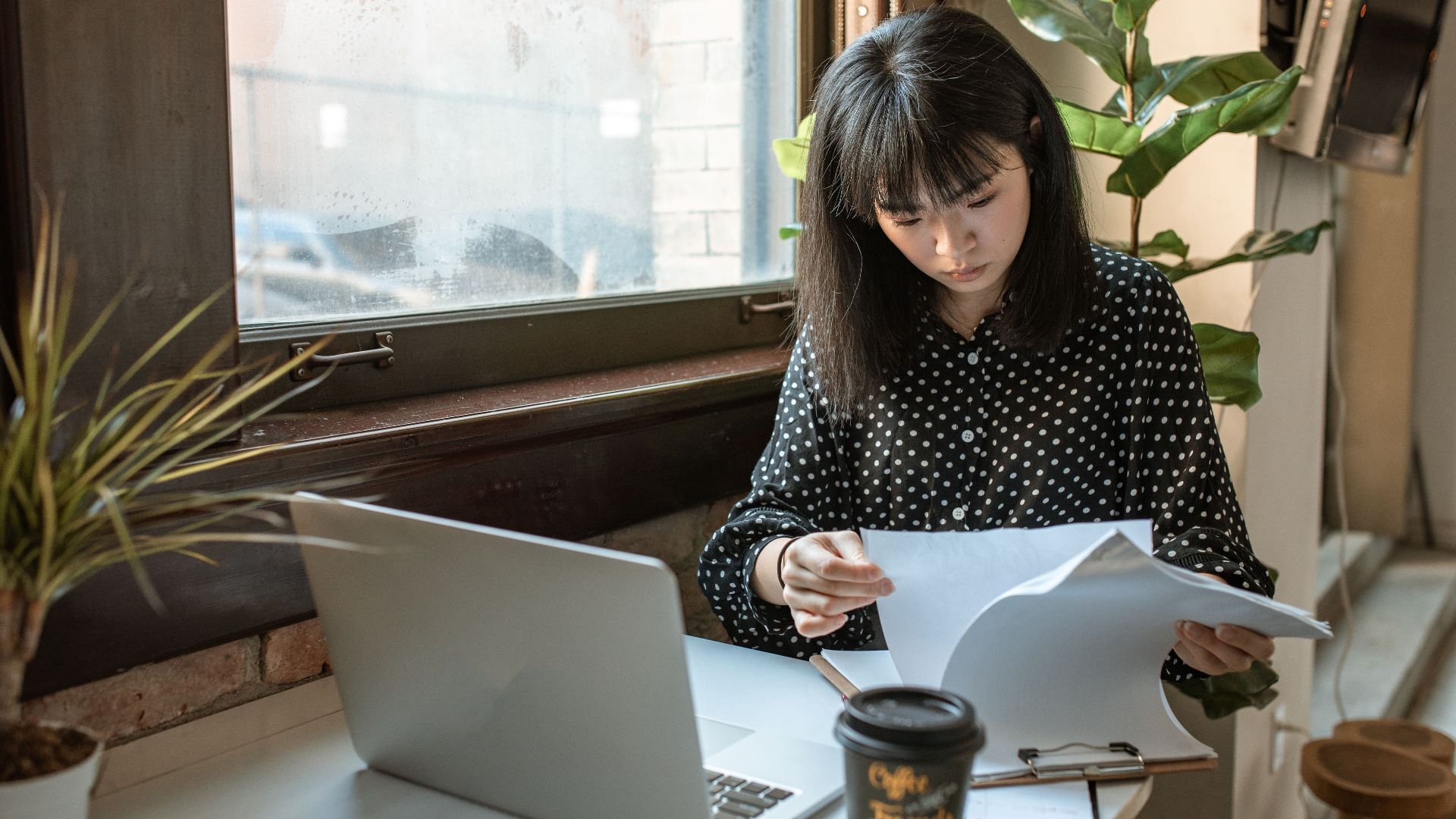 Asian businesswoman reviewing documents in a modern office setting with natural light.