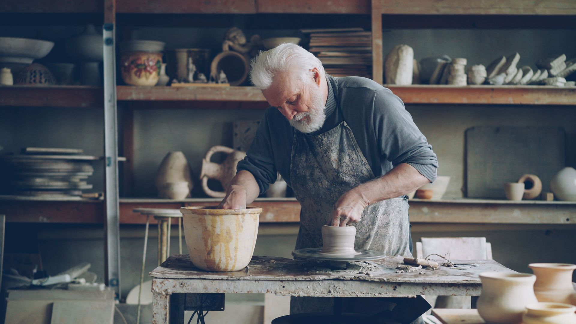 Senior male potter focused on shaping clay pottery in a traditional studio environment.