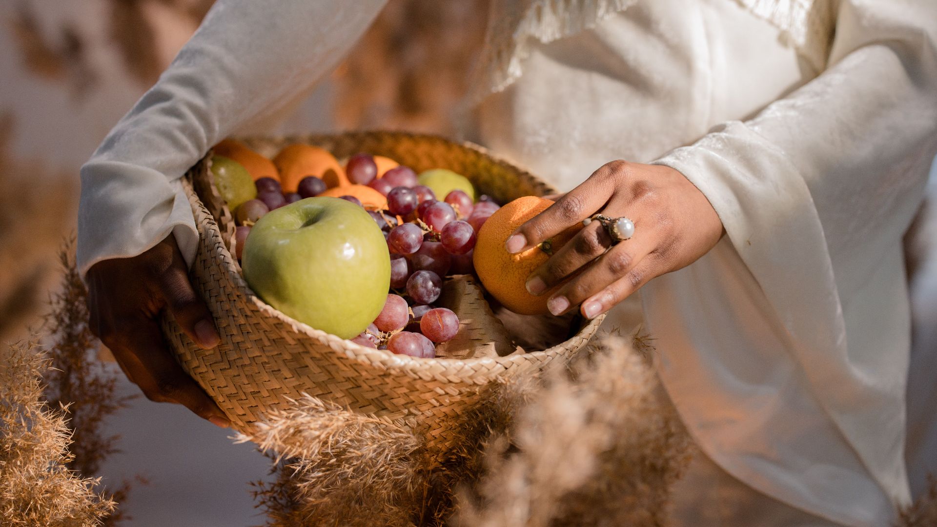 A close-up of hands holding a woven basket filled with various fresh fruits in natural light.